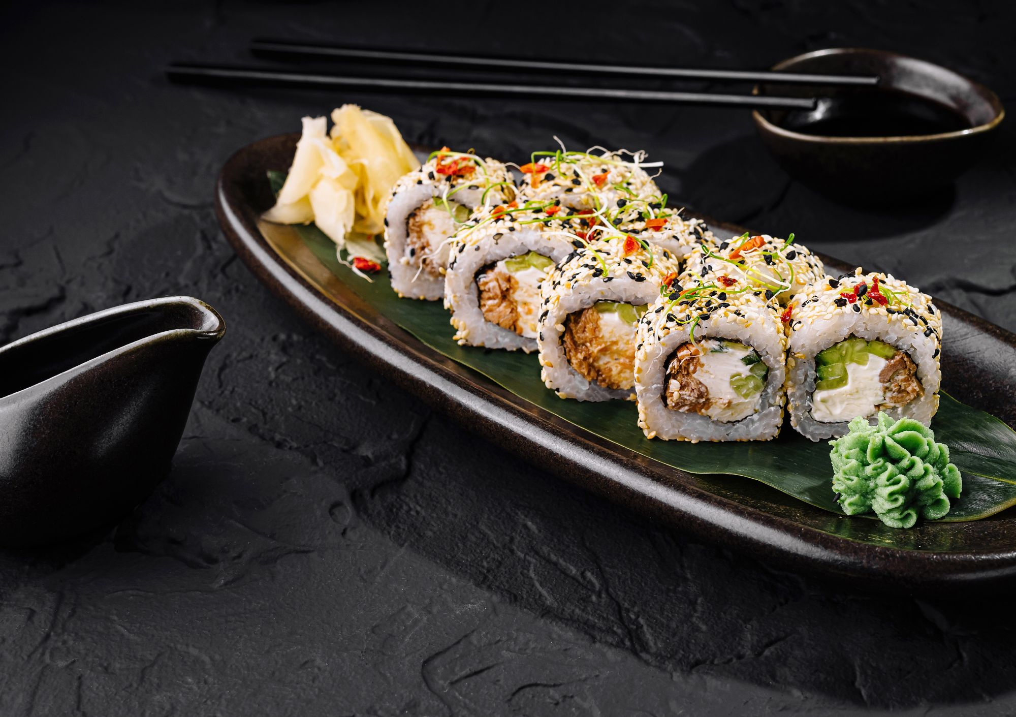Sushi na czarnej tacy z dodatkami, takimi jakwasabi, imbir i sos sojowy, idealne na japoński posiłek.
