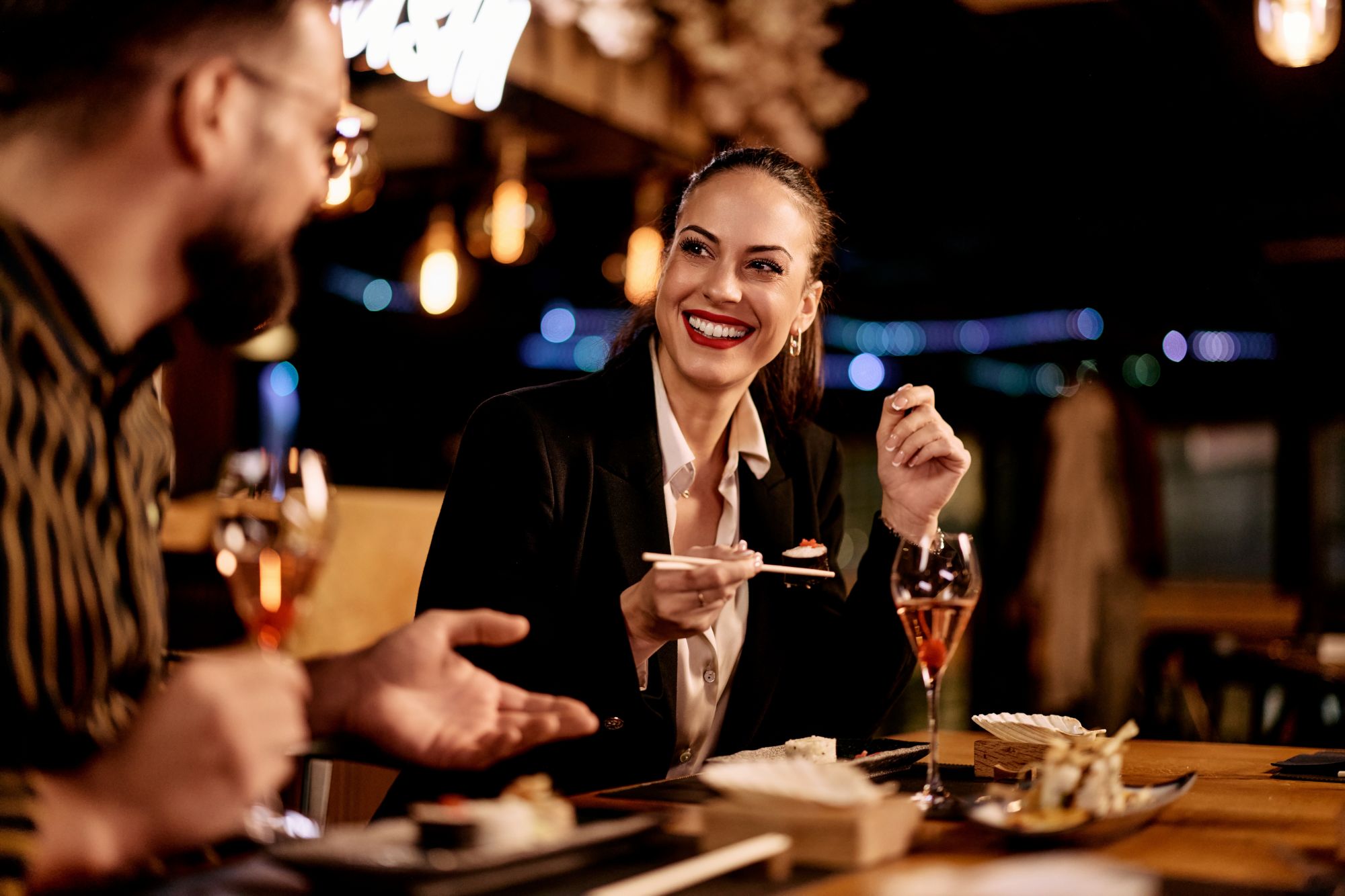 Dwójka osób uśmiecha się, jedząc sushi w przytulnej restauracji przy lampach.