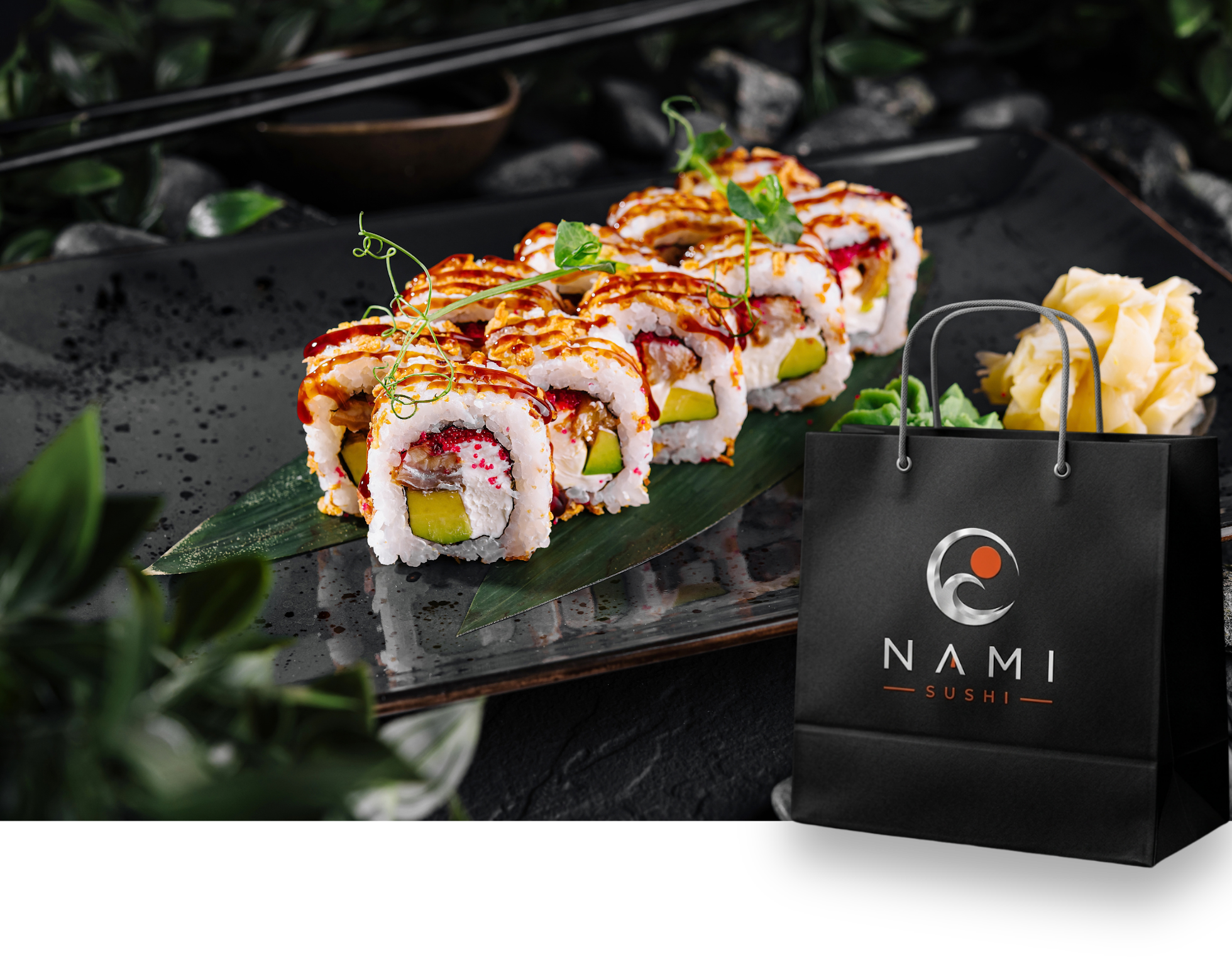 Sushi na czarnym talerzu z logo NAMI, obok elegancka torba na zakupy i liście dekoracyjne.