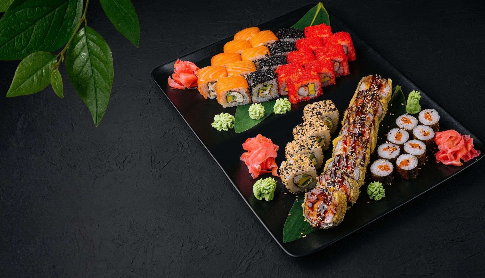 Talerz sushi z różnorodnymi rolkami, wasabi i marynowanym imbirem na ciemnym tle.