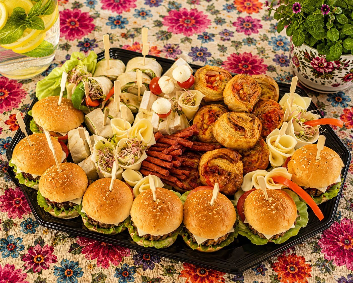 Tacka z różnorodnymi przekąskami: mini burgery, kanapki, tortille i różne sałatki.