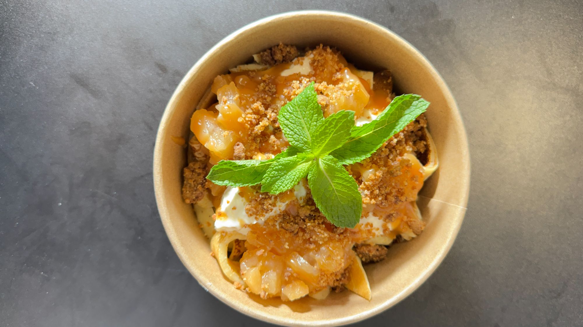 Pasta w misce z sosem owocowym, bitą śmietaną, kruszonką i świeżą miętą na wierzchu.