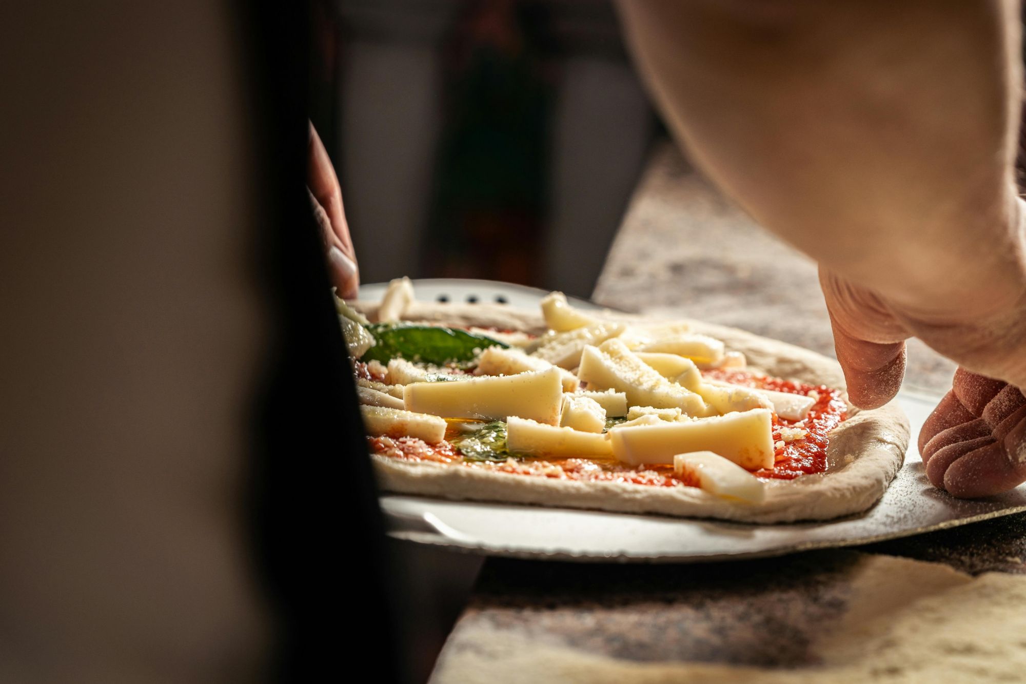 Ručne pripravovaná pizza s paradajkovým základom, syrom a bazalkou pred pečením.