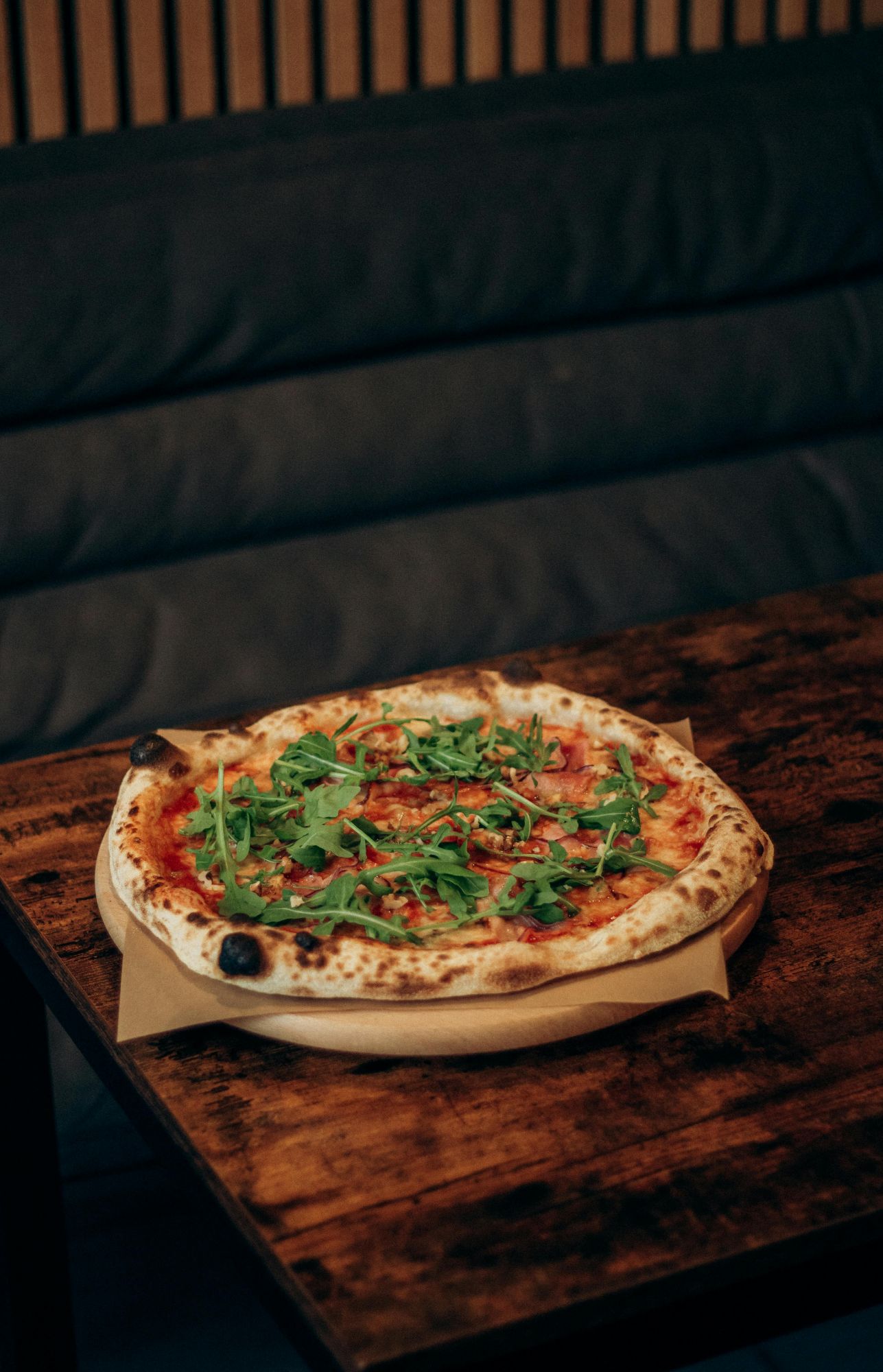 Pizza s paradajkovým základom, mozzarellou a čerstvou rukolou na drevenom stole.