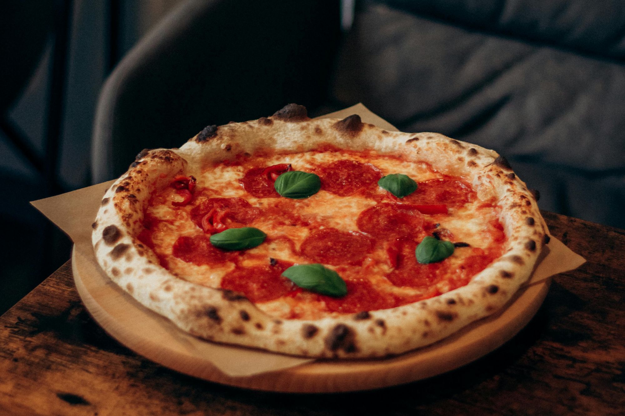 Kruhová pizza s pepperoni a bazalkou na drevenom podnose na stole.