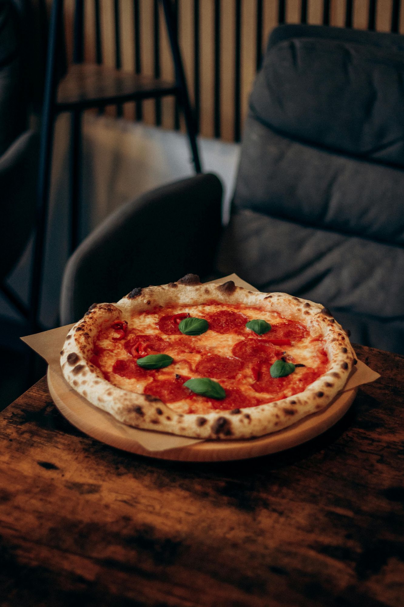 Pizza s pepperoni a bazalkou na drevenom tanieri na stole v reštaurácii.