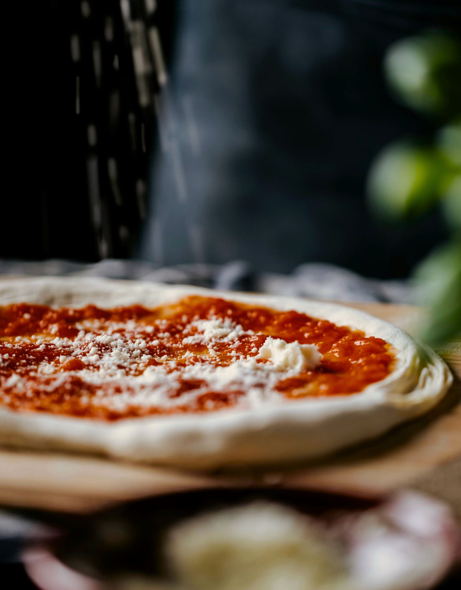 Pizza s paradajkovou omáčkou a syrom na drevenej doske, posypaná múkou.