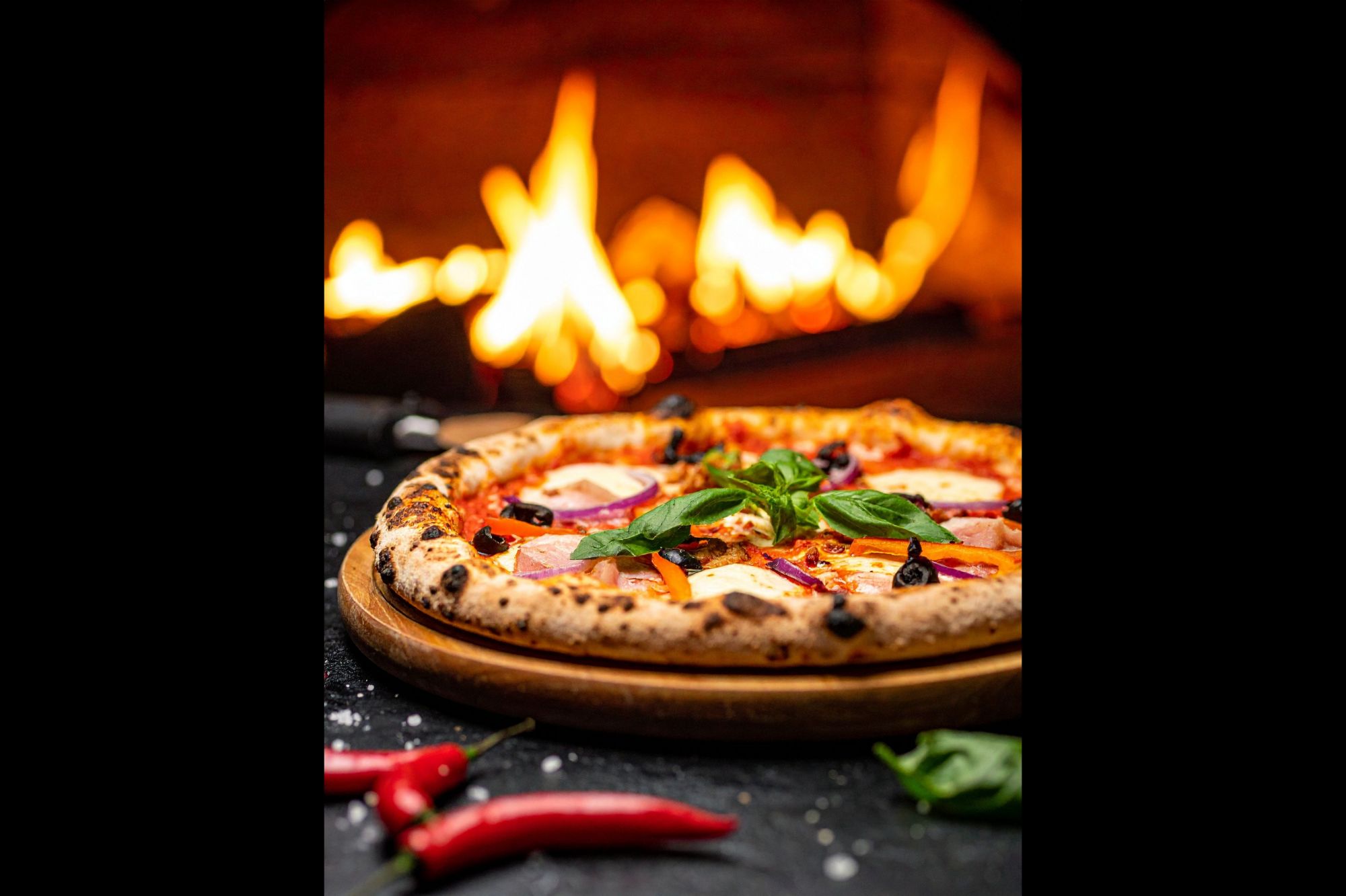 Pizza s rajčicom, maslinama i bosiljkom ispod vatre u pećnici.