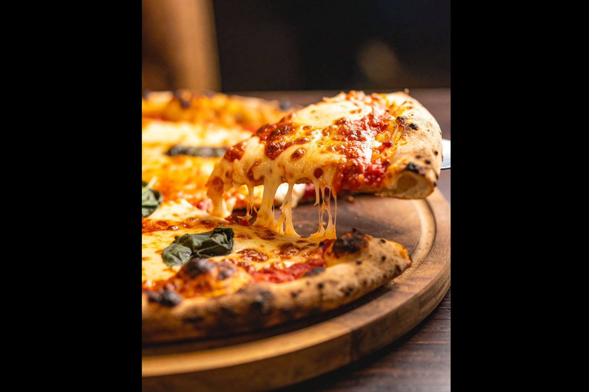 Povoljna pizza s rastopljenim sirom, rajčicom i svježim bosiljkom, izvučena iz pećnice na drvenoj podlozi.