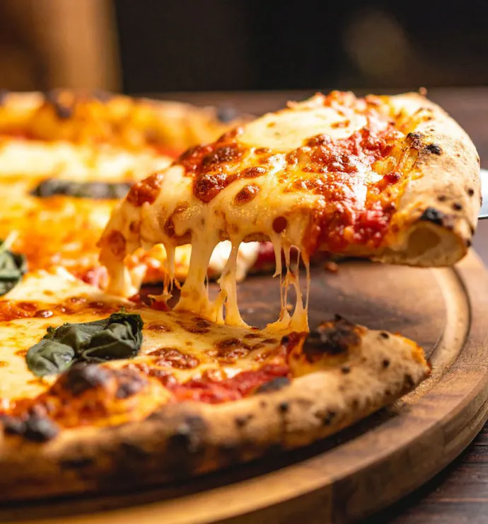Povoljna pizza s rastopljenim sirom, rajčicom i svježim bosiljkom, izvučena iz pećnice na drvenoj podlozi.