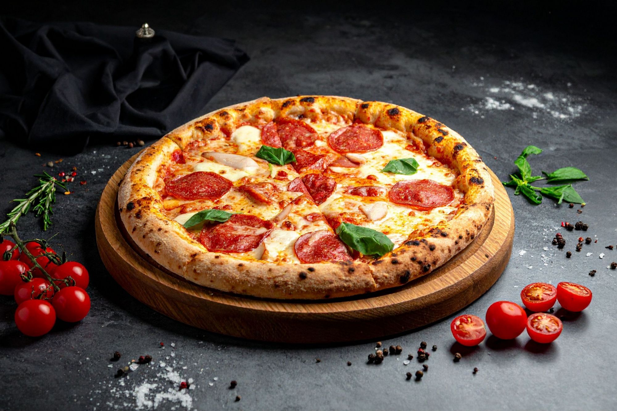 Pizza s pečenom salamu, mocarelom i svježim bosiljkom, poslužena na drvenoj dasci uz cherry rajčice i začine.
