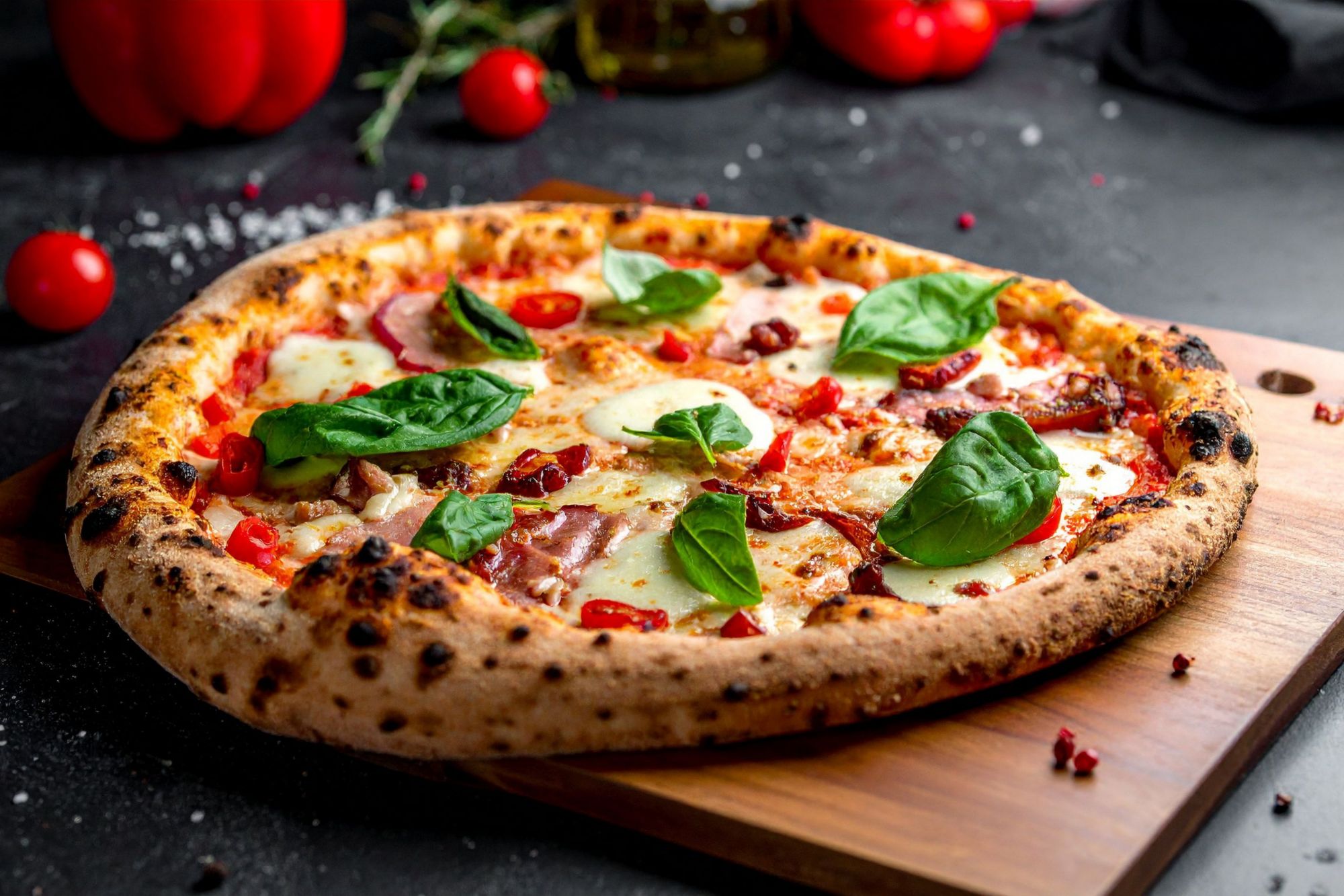 Pizza sa sirom, rajčicama, dimljenom slaninom i svježim bosiljkom, poslužena na drvenoj dasci.