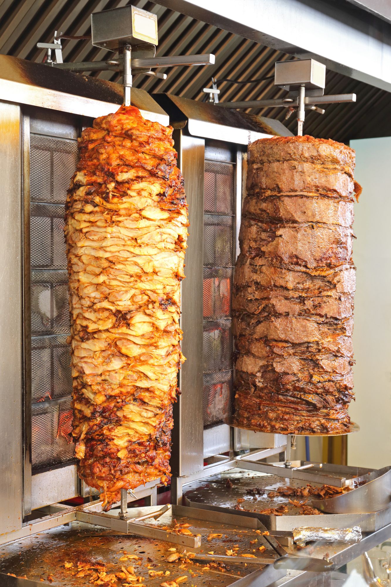 Obrazy dwóch pionowych rożnów: jeden z kurczaka, drugi z wołowiny, pieczonych na rożnie w restauracji.