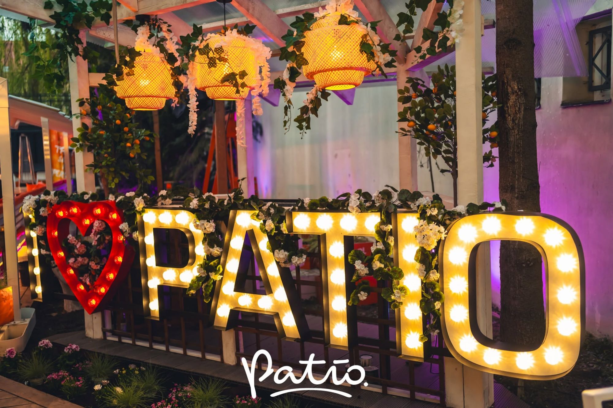 Zdobiona przestrzeń patio z podświetlonym napisem "I ♥ PATIO" i lampionami w tle.