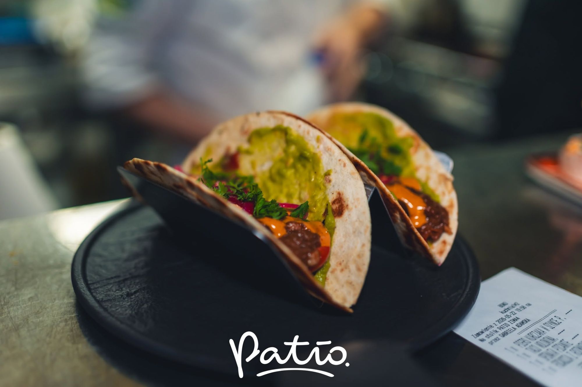 Dwie tacos na talerzu, wypełnione guacamole, warzywami i sosem, w restauracji Patio.