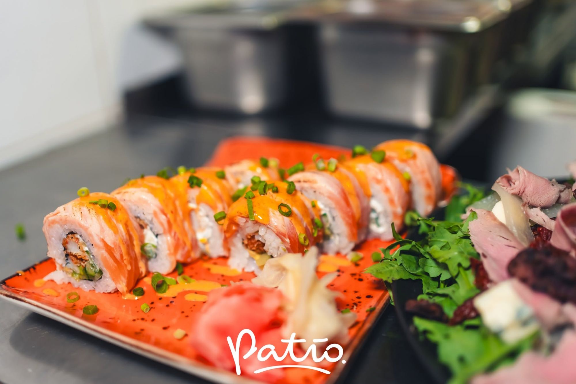Sushi na pomarańczowym talerzu, z łososiem i szczypiorkiem, obok sałata i dodatki w restauracji.