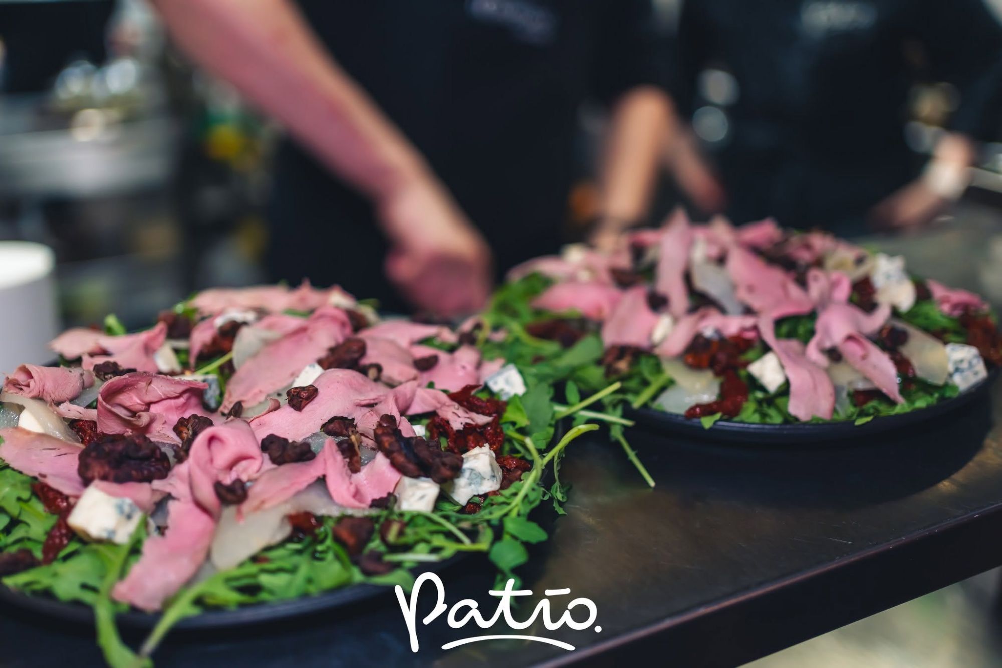 Sałatka z rukolą, dużą ilością mięsa i serem, podana na czarnych talerzach w restauracji Patio.