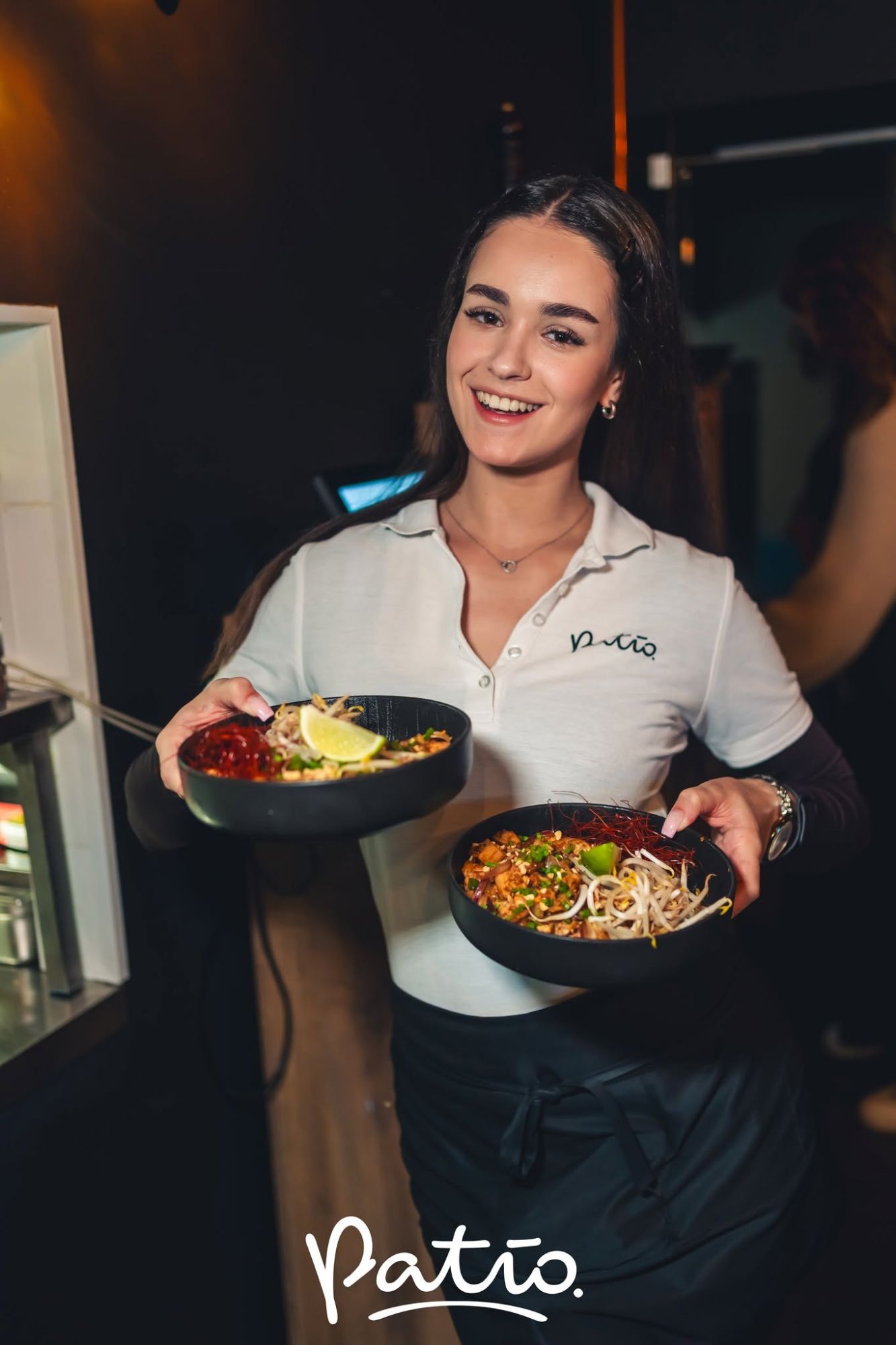 Kelnerka w białej koszuli trzyma dwa talerze z jedzeniem w restauracji Patio.