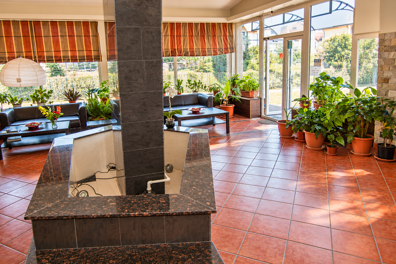Interior primitor cu canapele confortabile, plante verzi și o fântână în centrul unei camere luminoase.