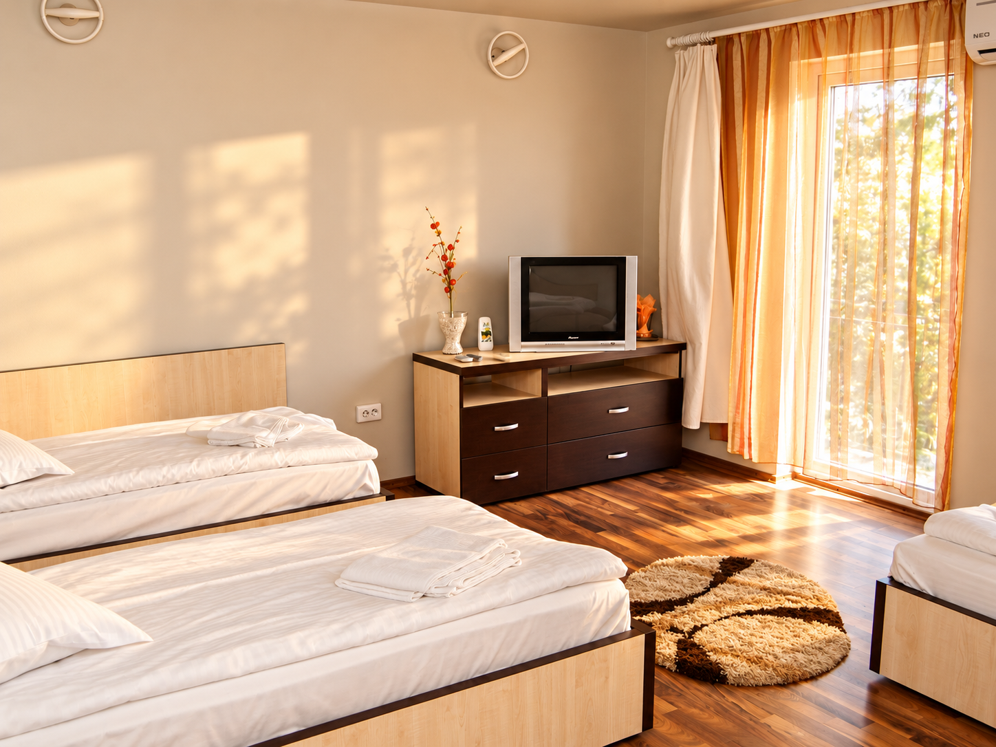 Camera de hotel luminoasă, cu două paturi, televizor, fereastră mare și draperii elegante.