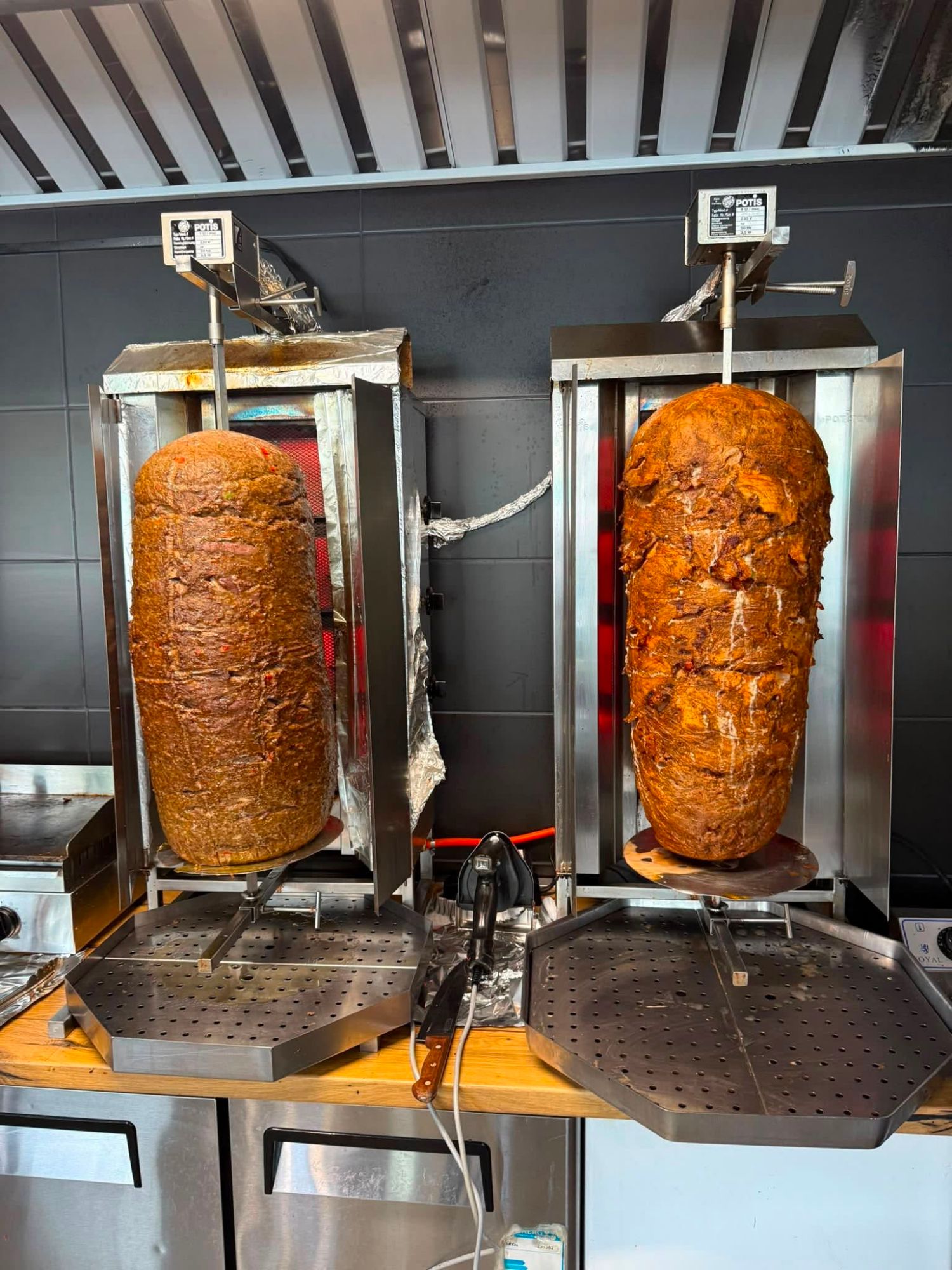 Dwa rożna do kebabu, jedno z mięsem drobiowym, drugie z wieprzowym, w lokalu gastronomicznym.