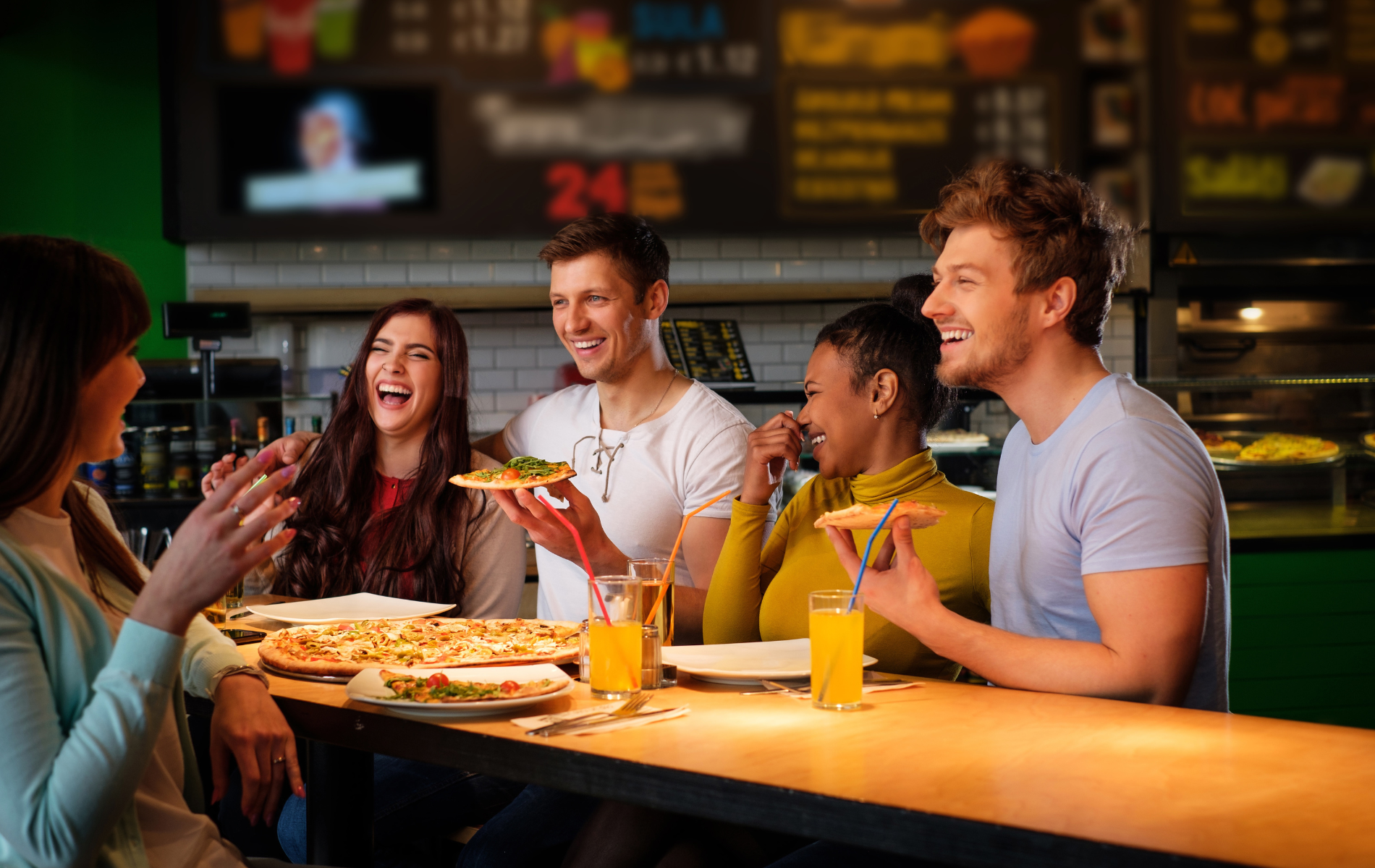 Grupa przyjaciół bawi się przy stole, jedząc pizzę i napoje w przytulnej restauracji.