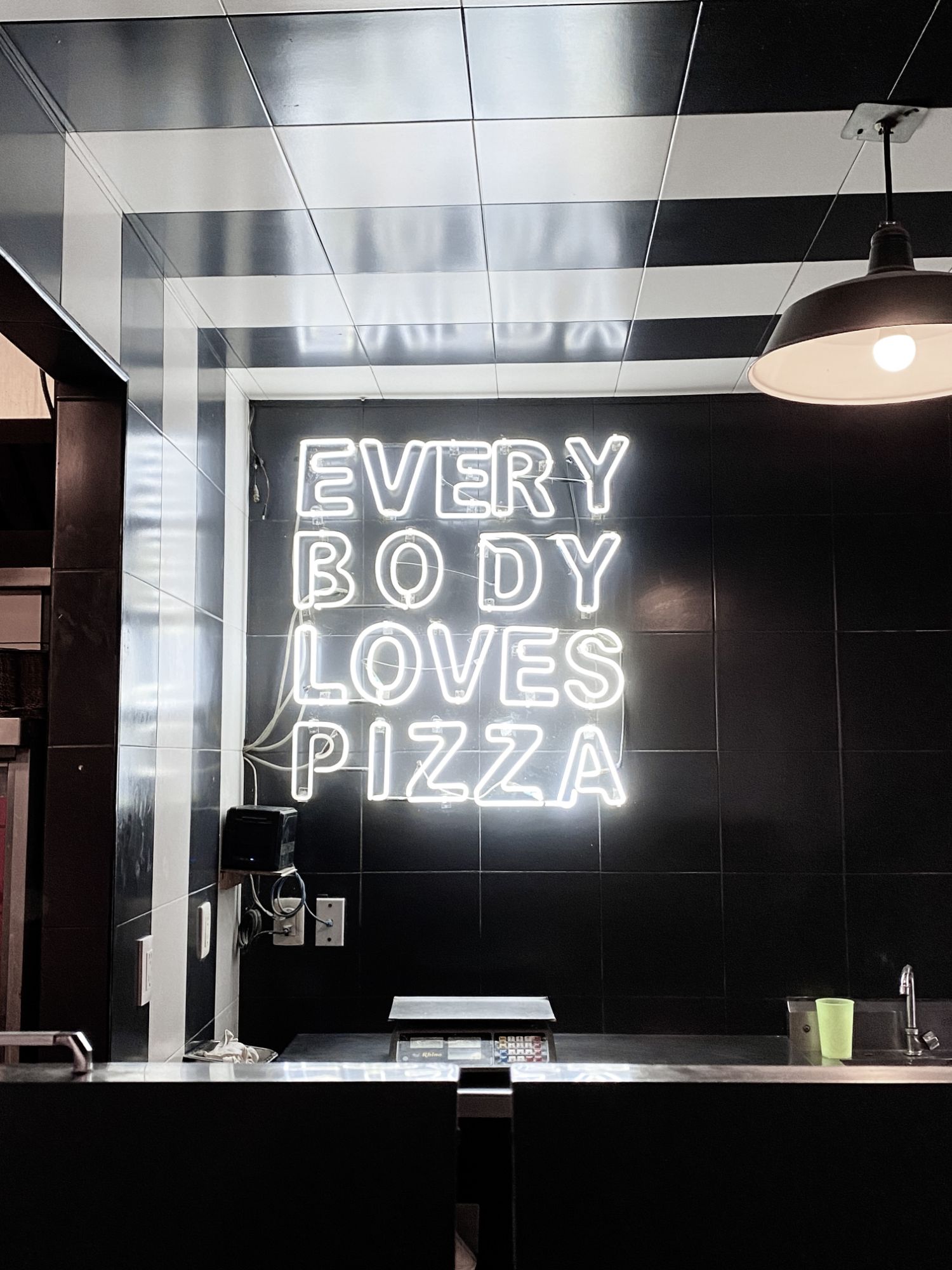 Neónový nápis „Každý miluje pizzu“ na čiernej stene v modernom interiéri reštaurácie.