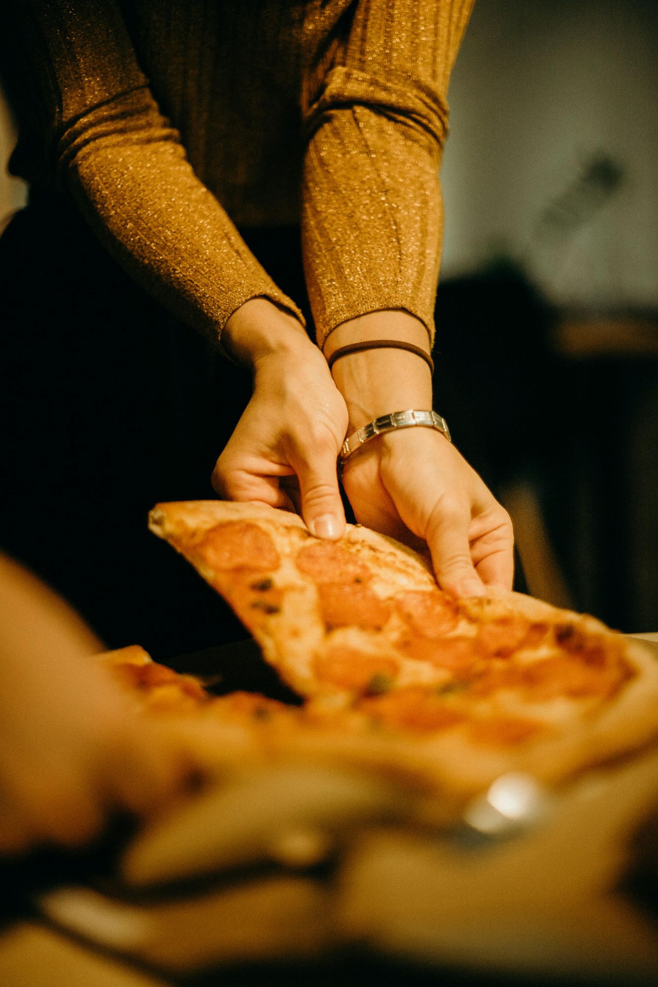 Ruka podáva kus pizze zo stola, na ktorom sú ďalšie kusy a príbor.