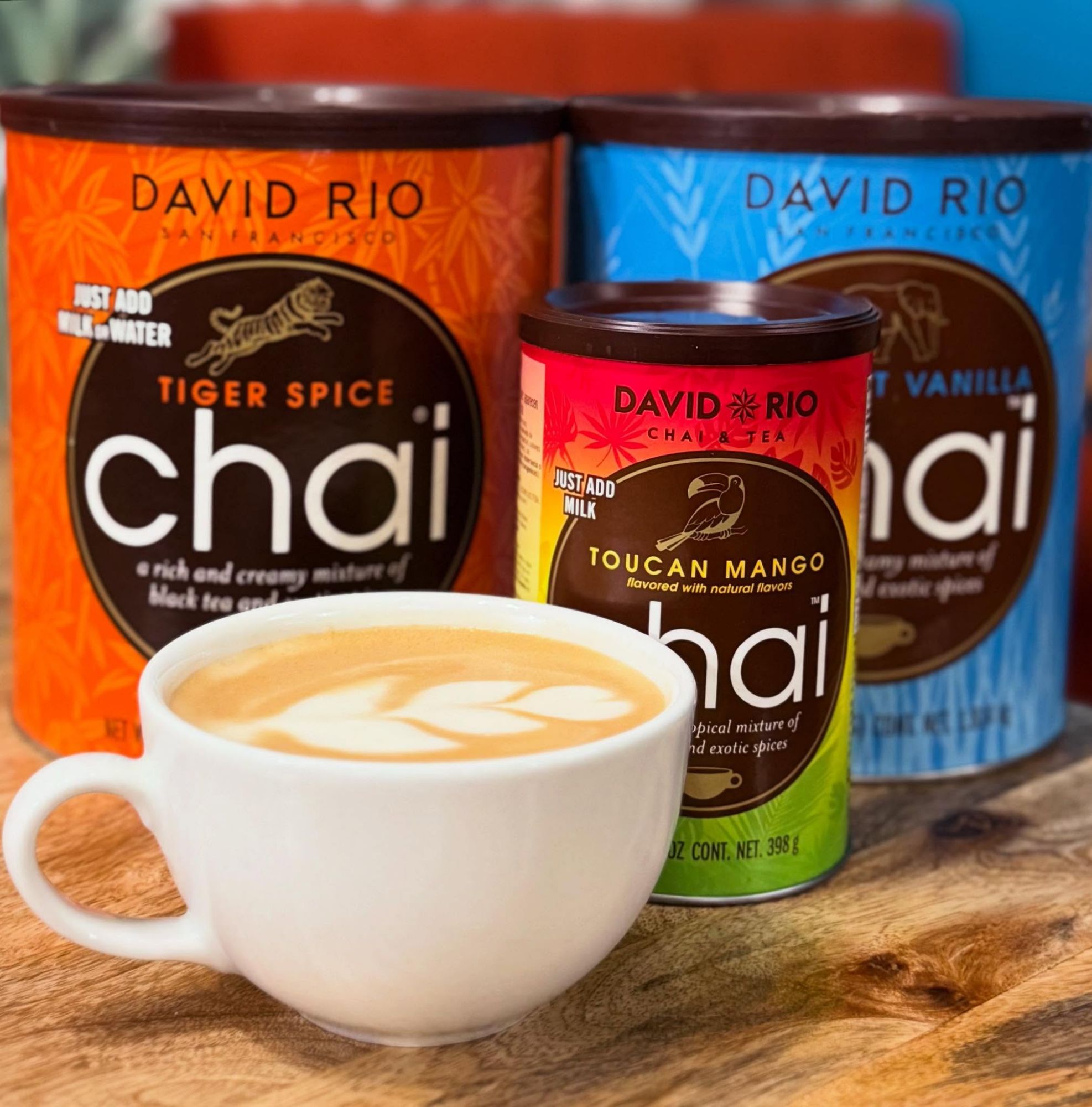 Kubek z chai i puszki herbaty David Rio: Tiger Spice, Vanilla i Toucan Mango na drewnianym stole.