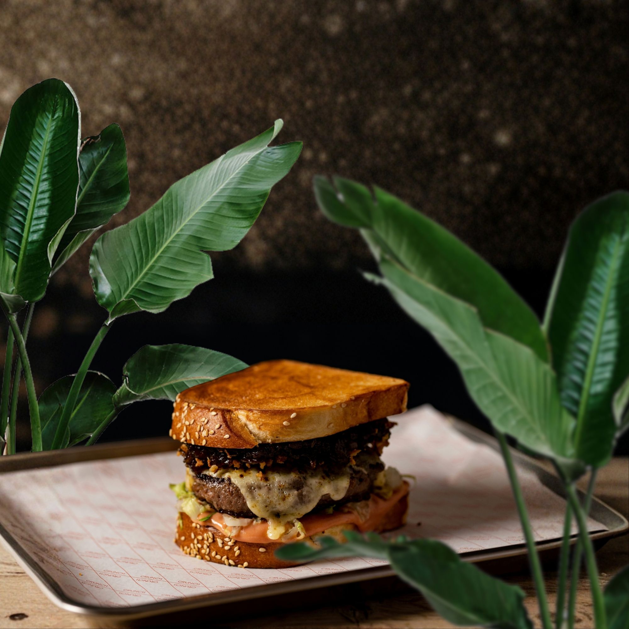 Soczysty burger z sałatą, pomidorem i serem, podany na złotej tacy w otoczeniu zielonych liści.