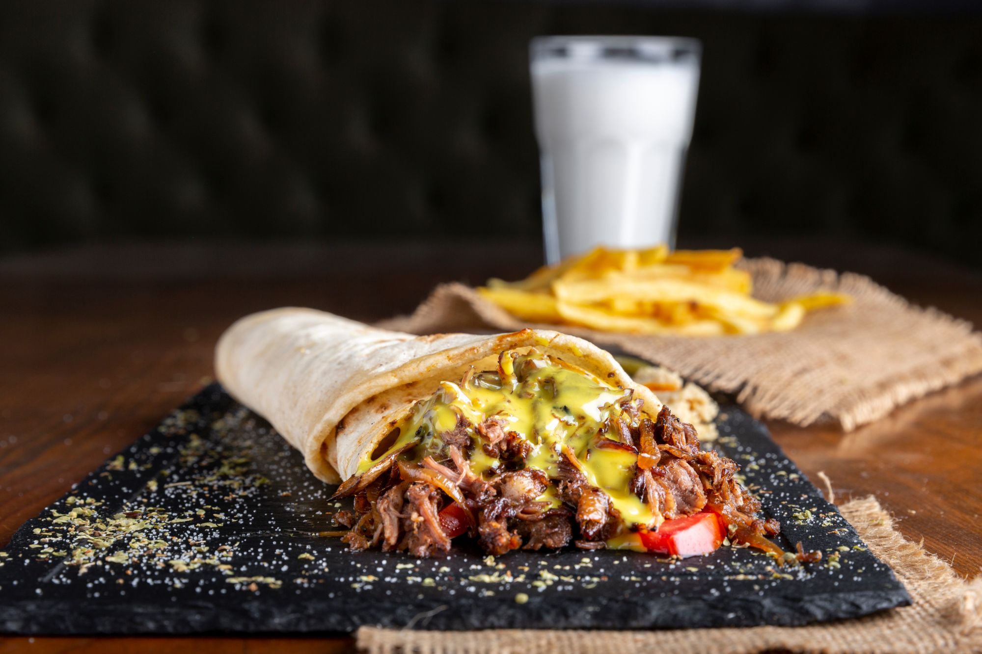 Wielki burrito z mięsem, serem, warzywami, z frytkami i szklanką mleka w tle na drewnianym stole.