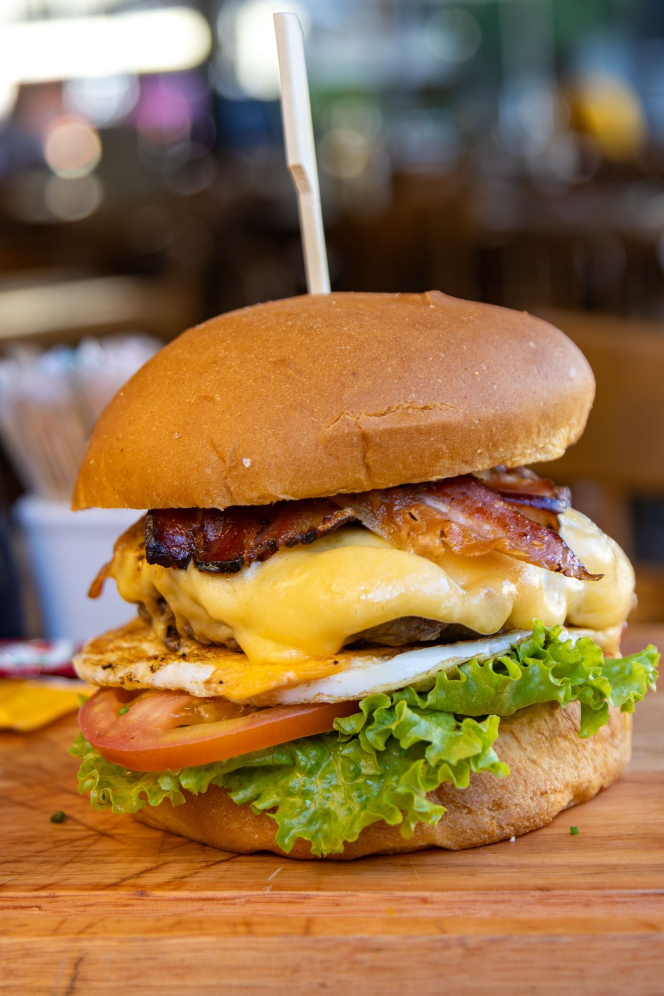 Burger z serem, bekonem, sałatą, pomidorem i grillowanym kurczakiem w bułce.