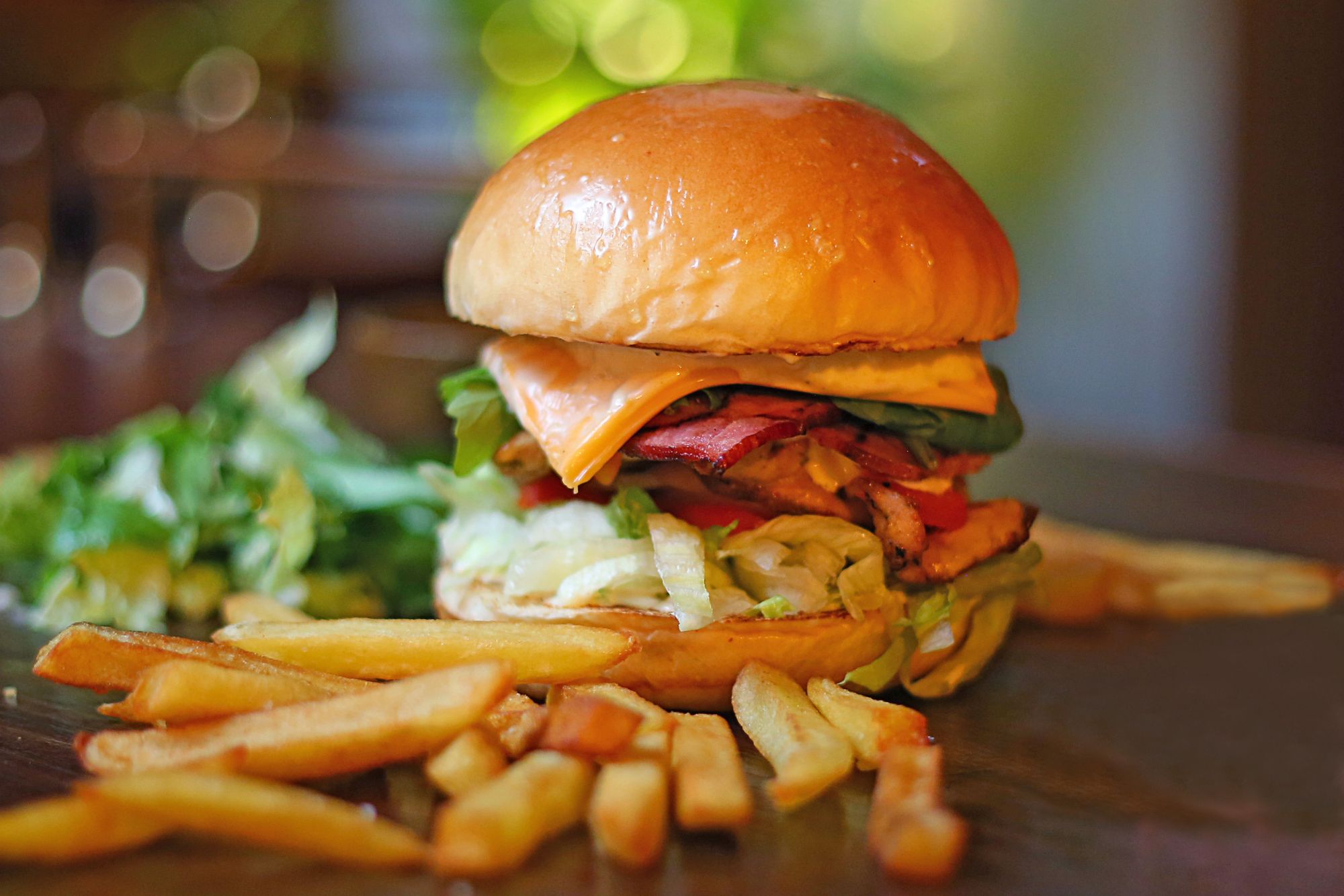 Burger z serem, warzywami i frytkami na talerzu.