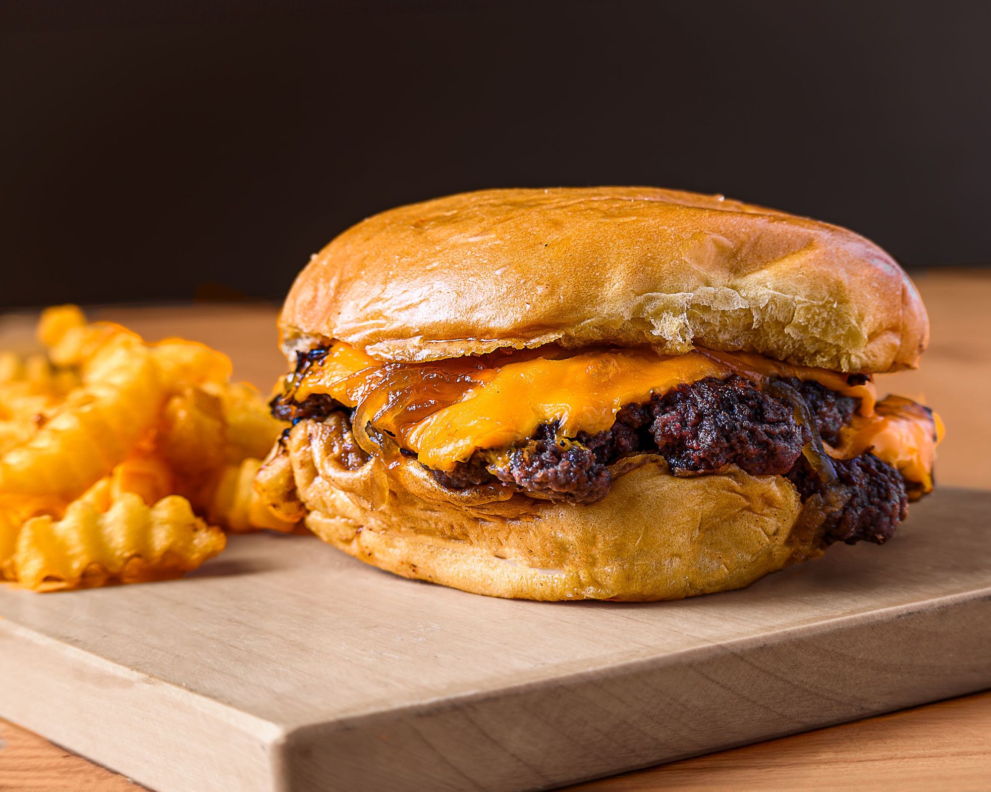 Burger z serem cheddar na złotym bułce, podany z frytkami w kształcie spirali.