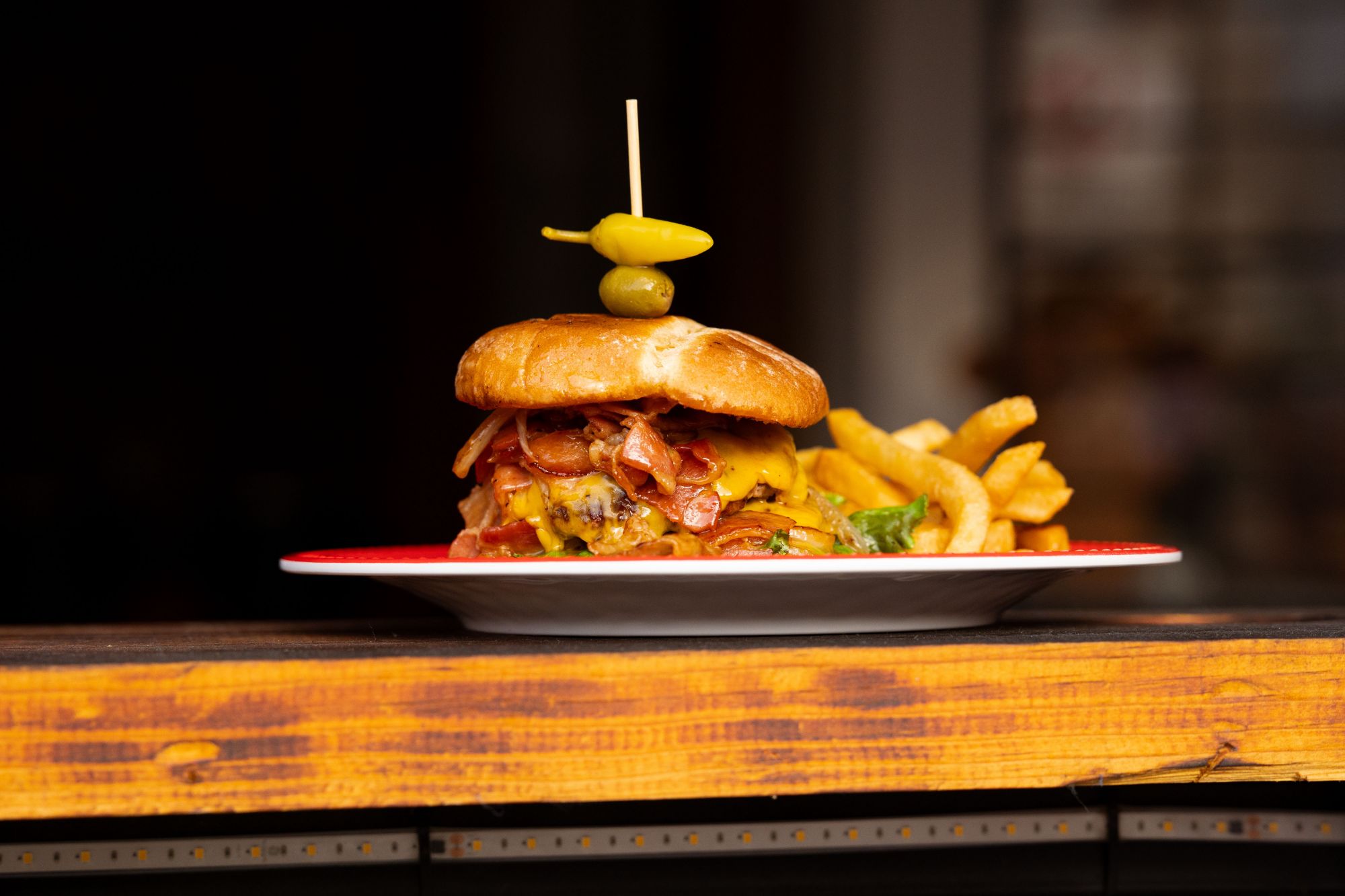 Soczysty burger z bekonem, serem, sałatą i oliwką, podany z frytkami.