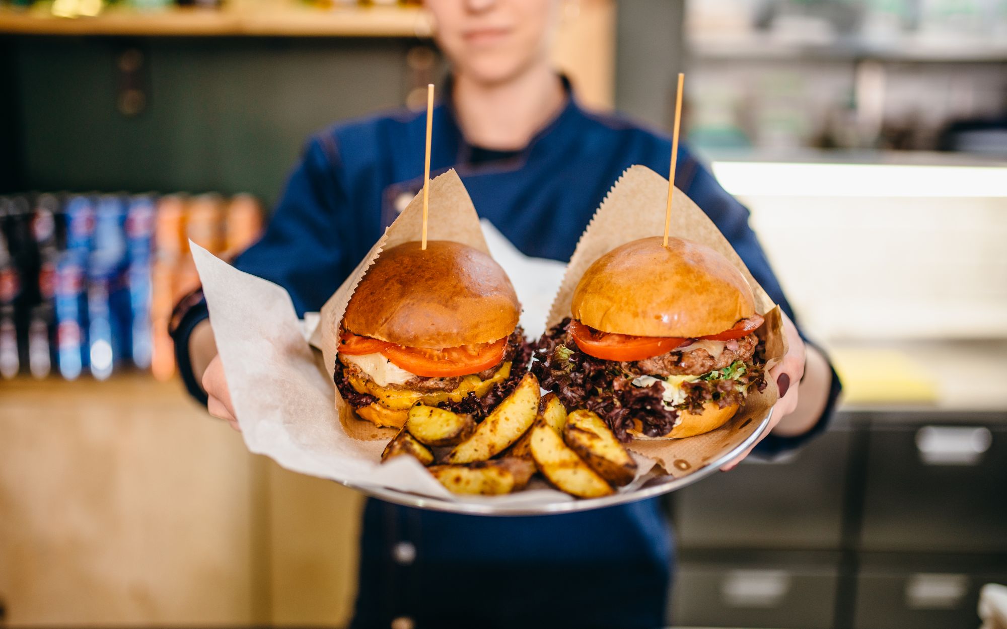 Kucharz trzyma talerz z dwoma burgerami i frytkami, podając je w restauracji.
