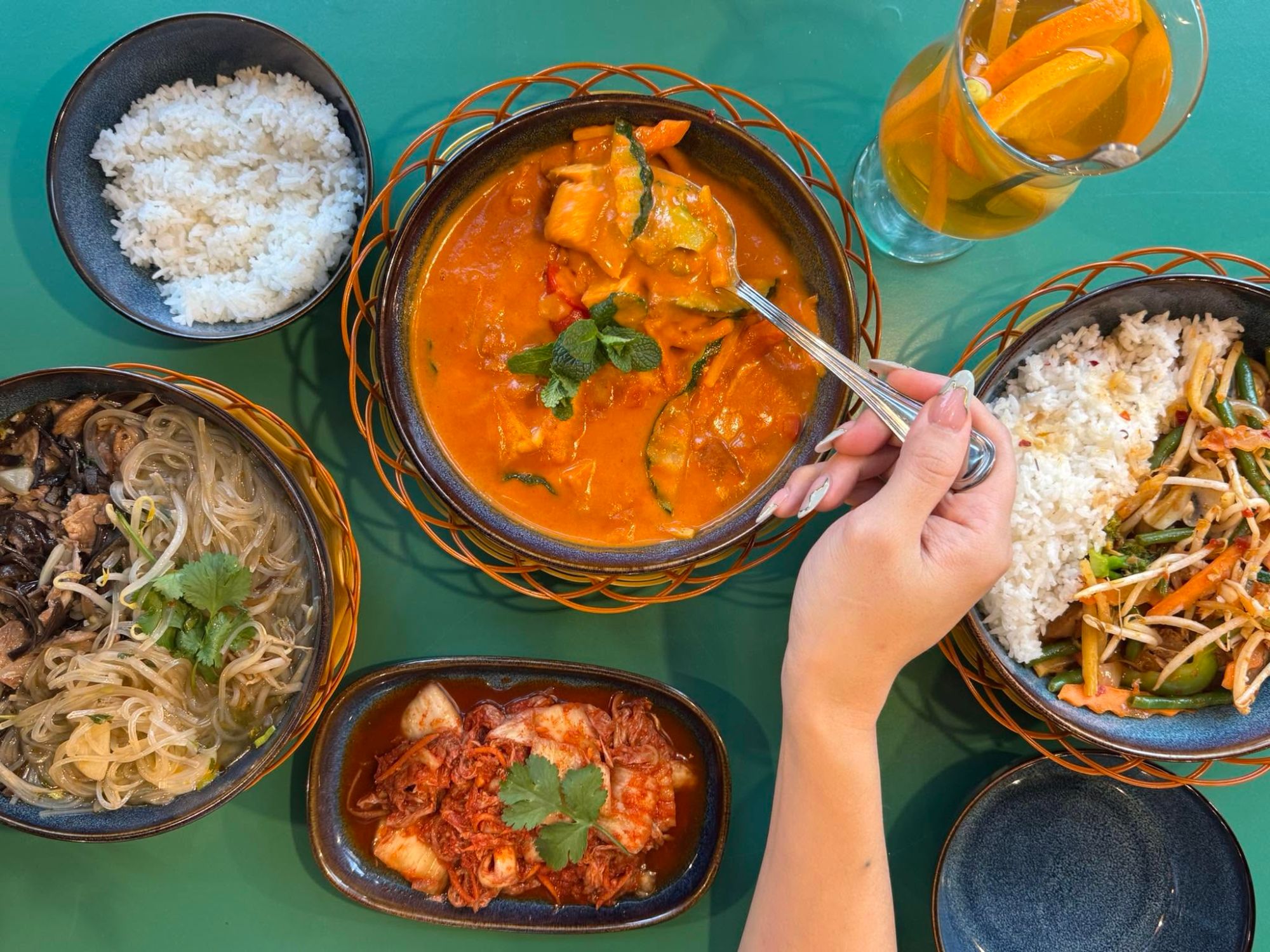 Obiad składający się z ryżu, curry, makaronu, sałatki oraz napoju w kolorowym zestawie talerzy.