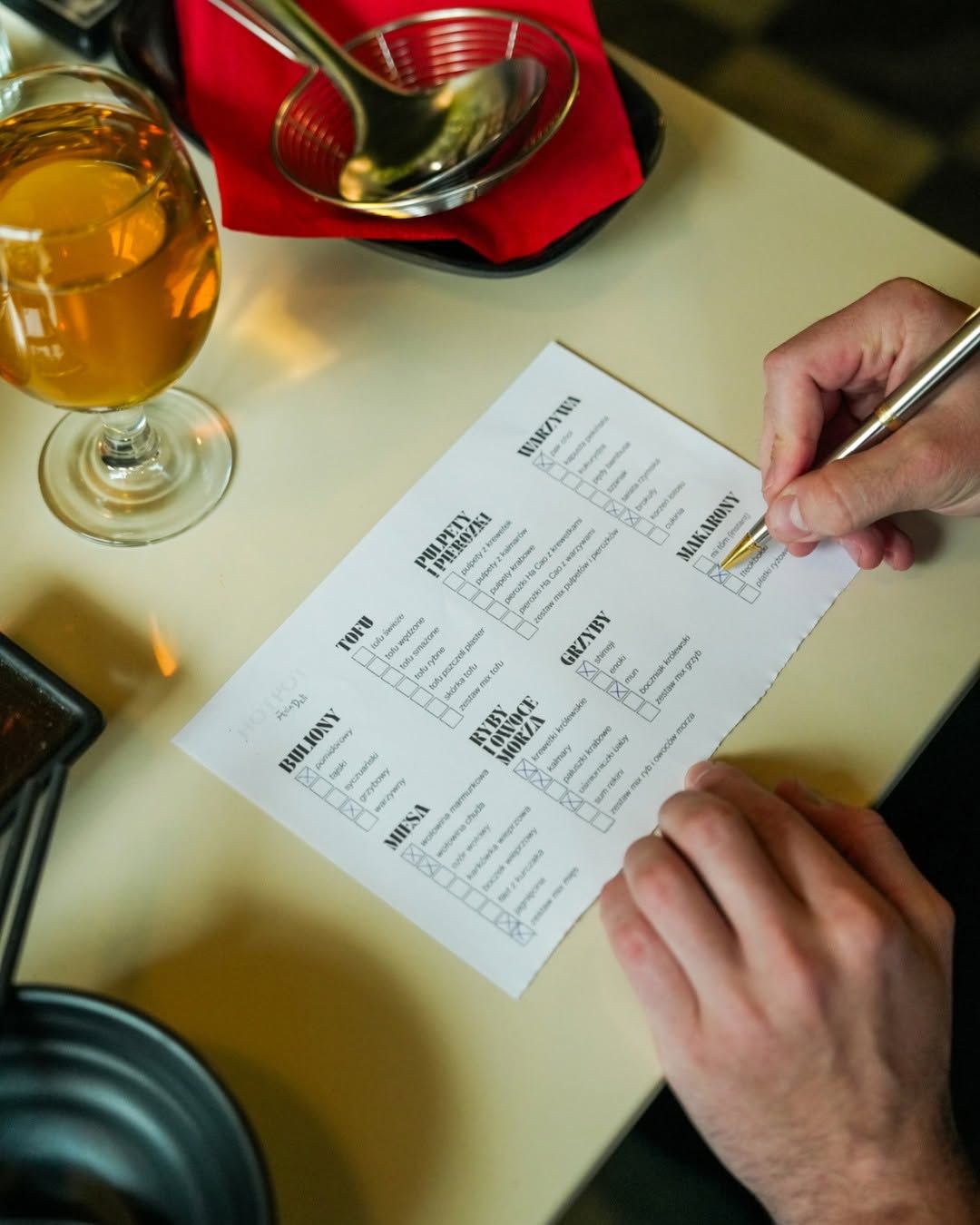 Mężczyzna zaznacza wybory na karcie zamówienia w restauracji, obok szklanka piwa i naczynia na stole.