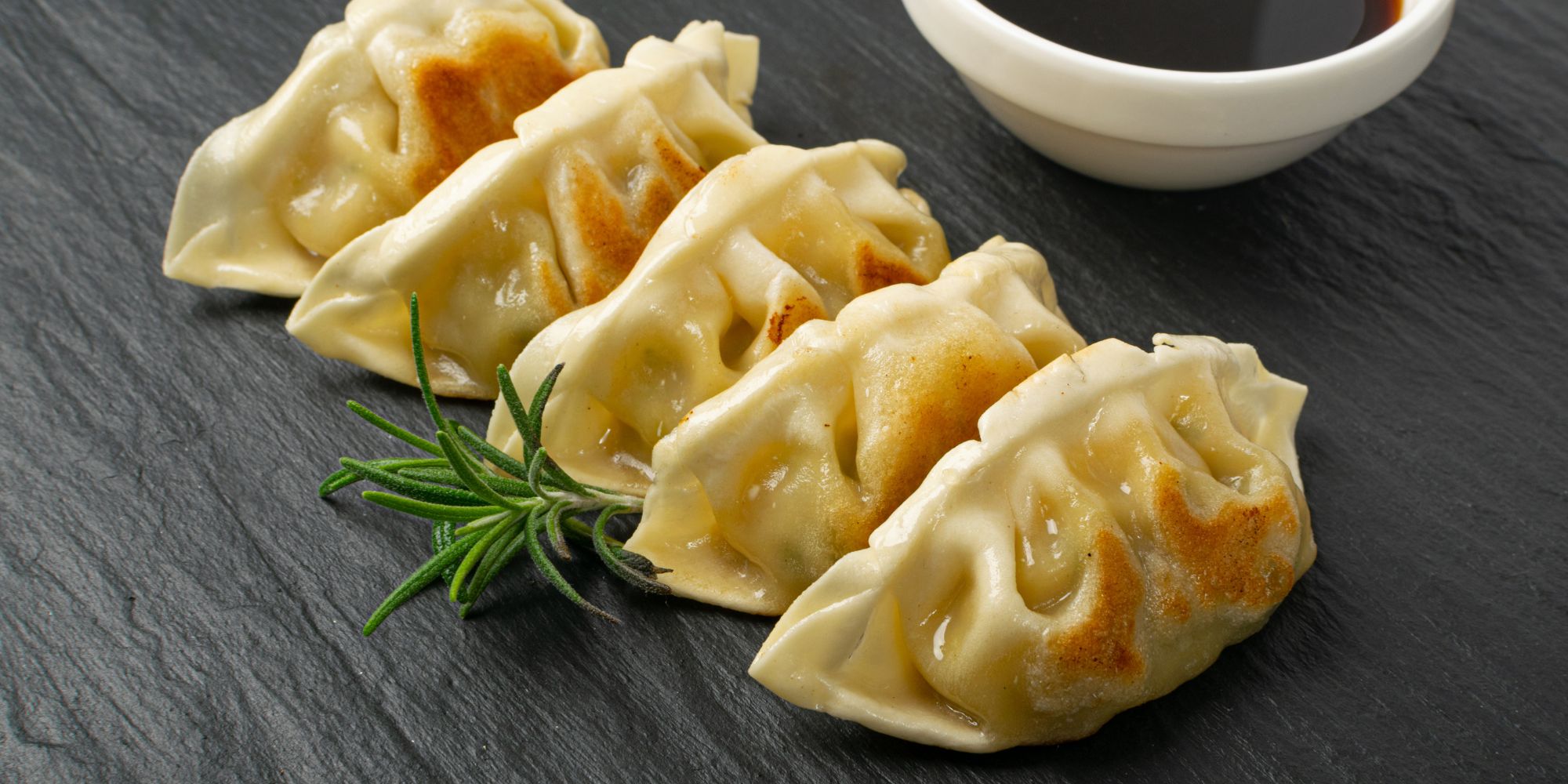 Pierogi ruskie podane na czarnym talerzu, z sosem sojowym i gałązką rozmarynu.