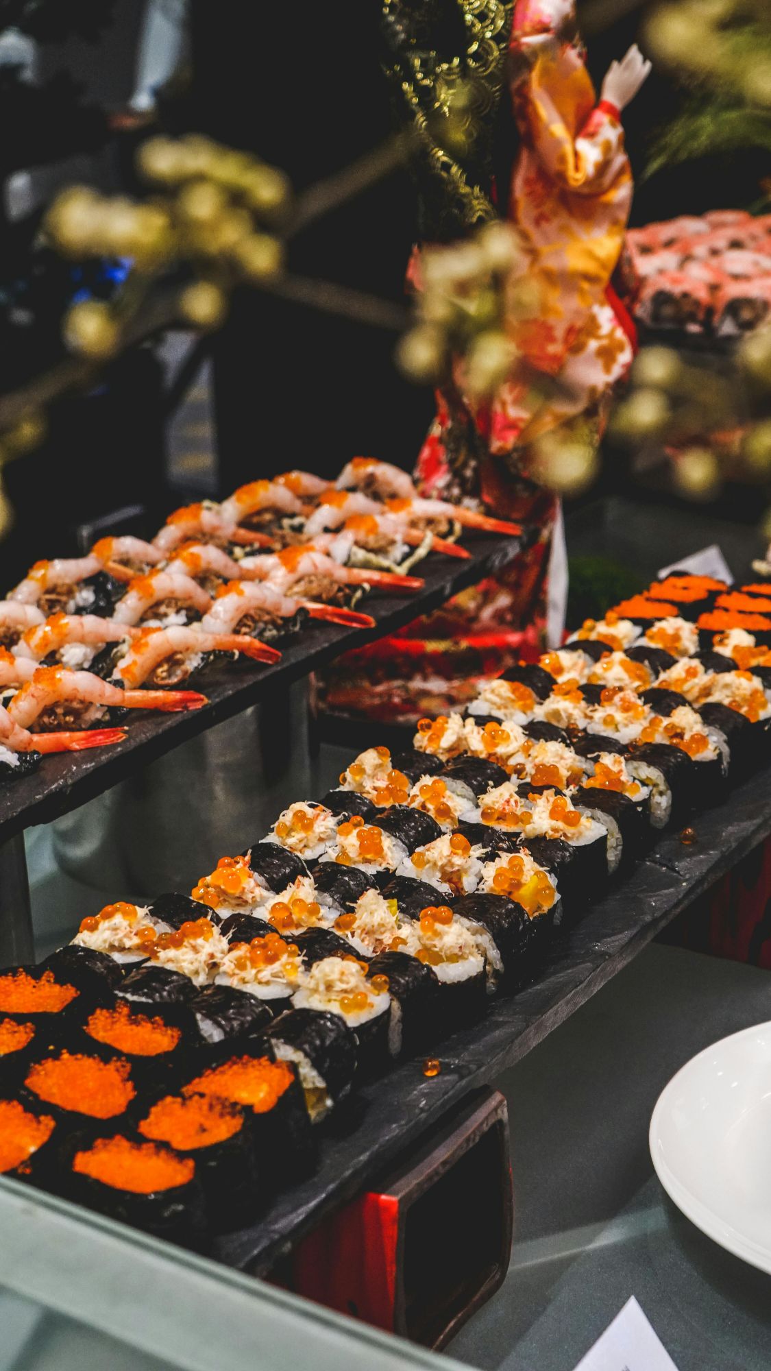 Różnorodne rolki sushi na tacy, z łososiem, krewetkami i ikrą, podane na eleganckim przyjęciu.