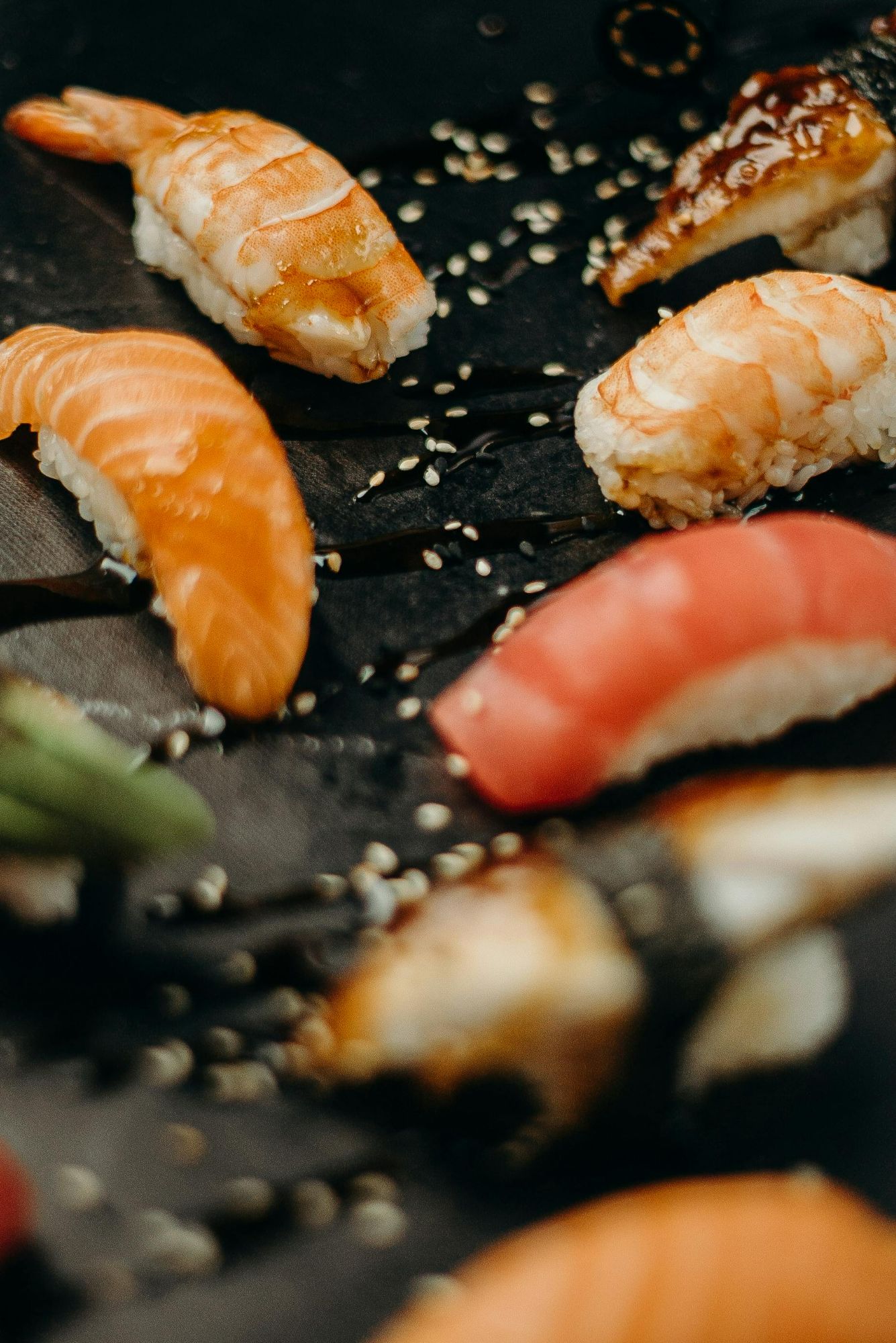 Sushi z różnymi rodzajami ryb na czarnym tle, posypane sezamem.