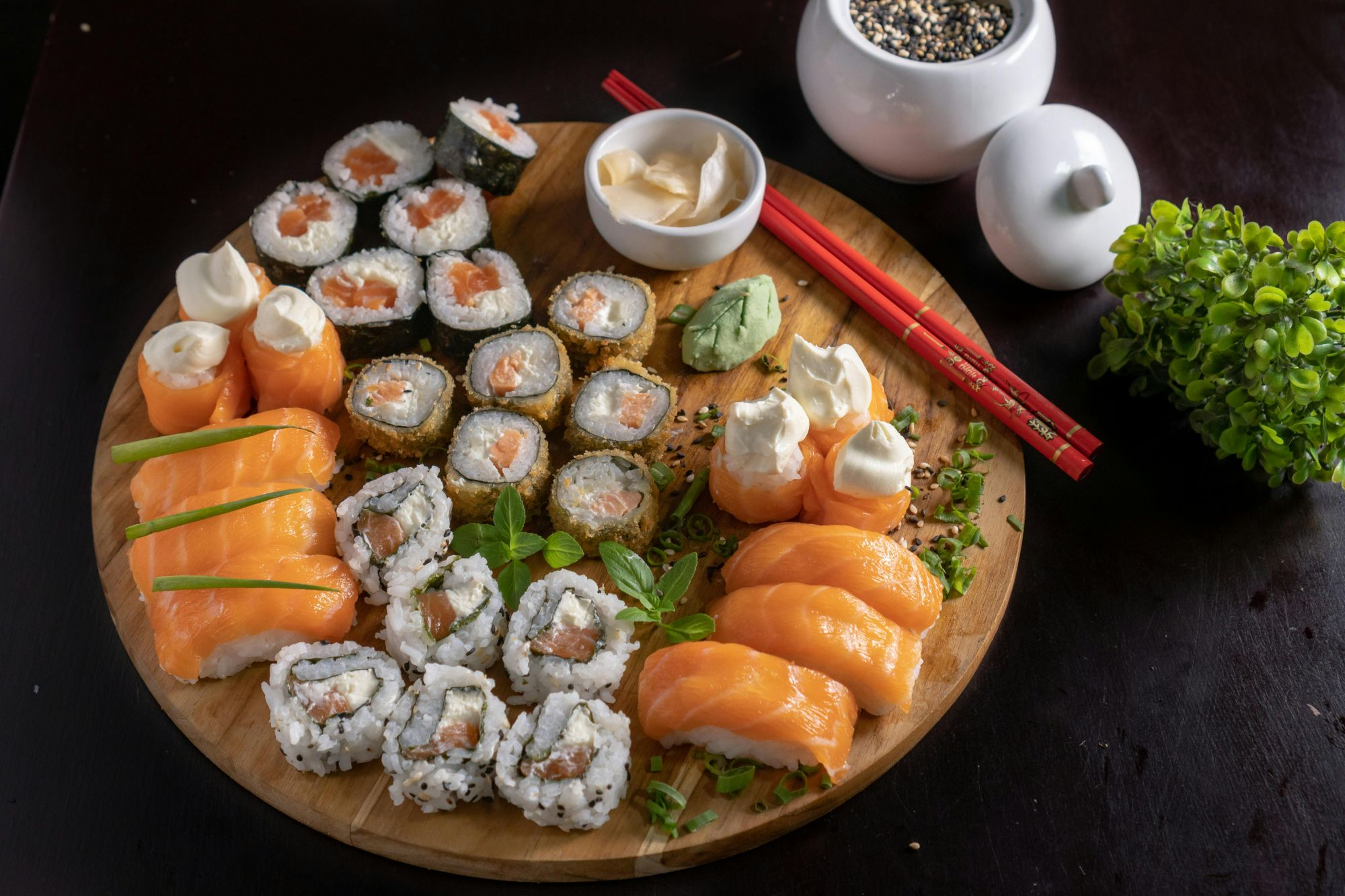 Talerz sushi z różnymi rolkami, w tym łososiem, wasabi i sosami, podany z pałeczkami.