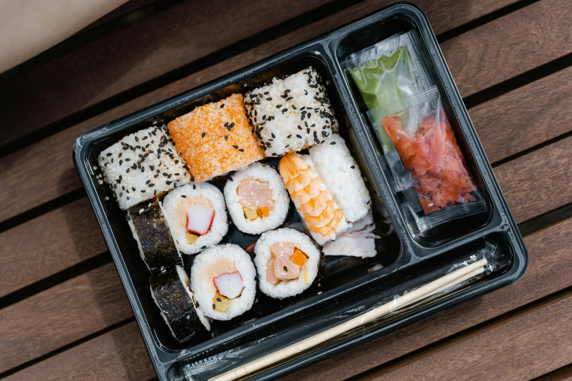 Sushi w plastikowym pojemniku, różne rolki, ryż, wodorosty, sos sojowy i marynowany imbir.