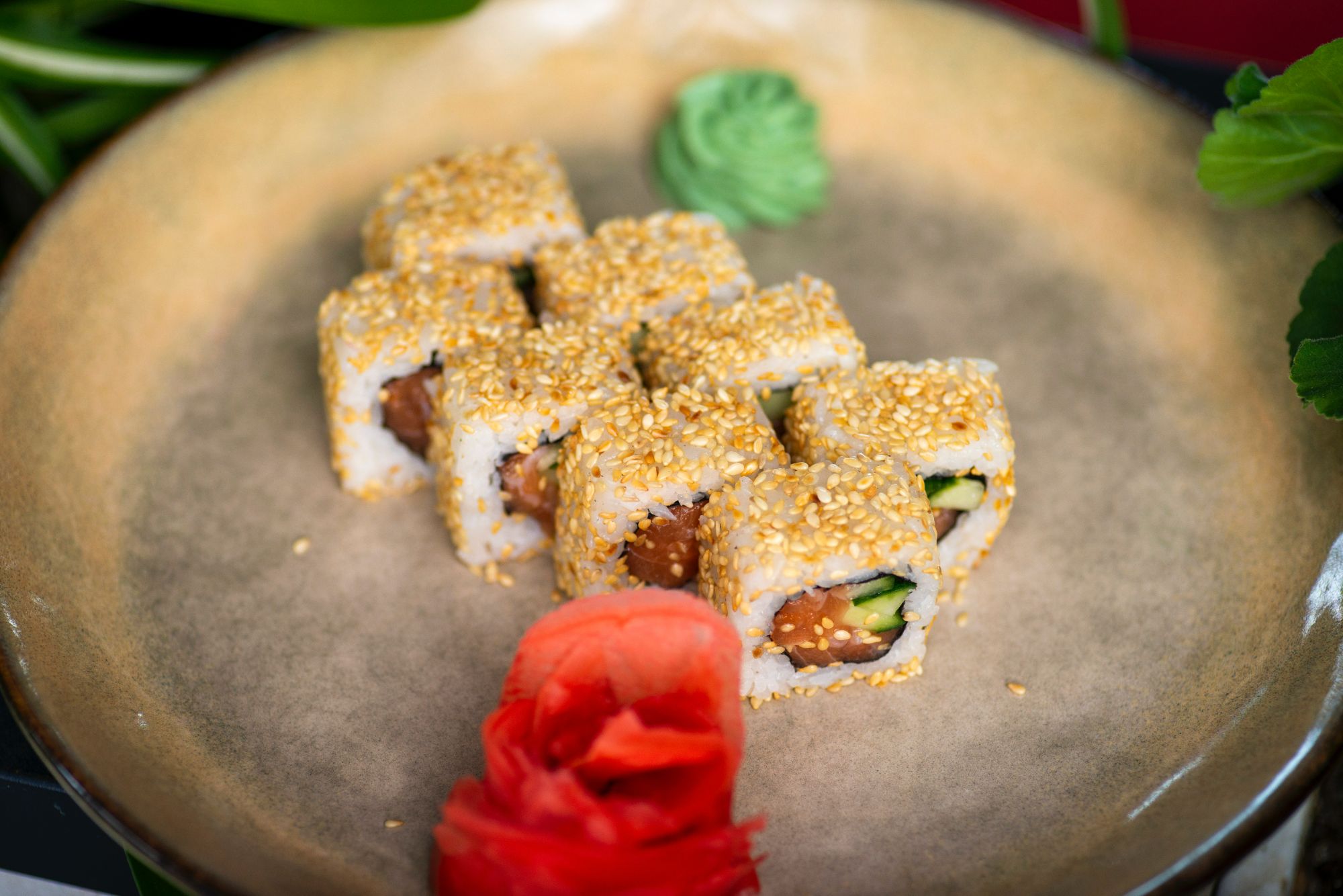 Zestaw sushi w sezamie na talerzu, z wasabi i różowym imbirze obok.