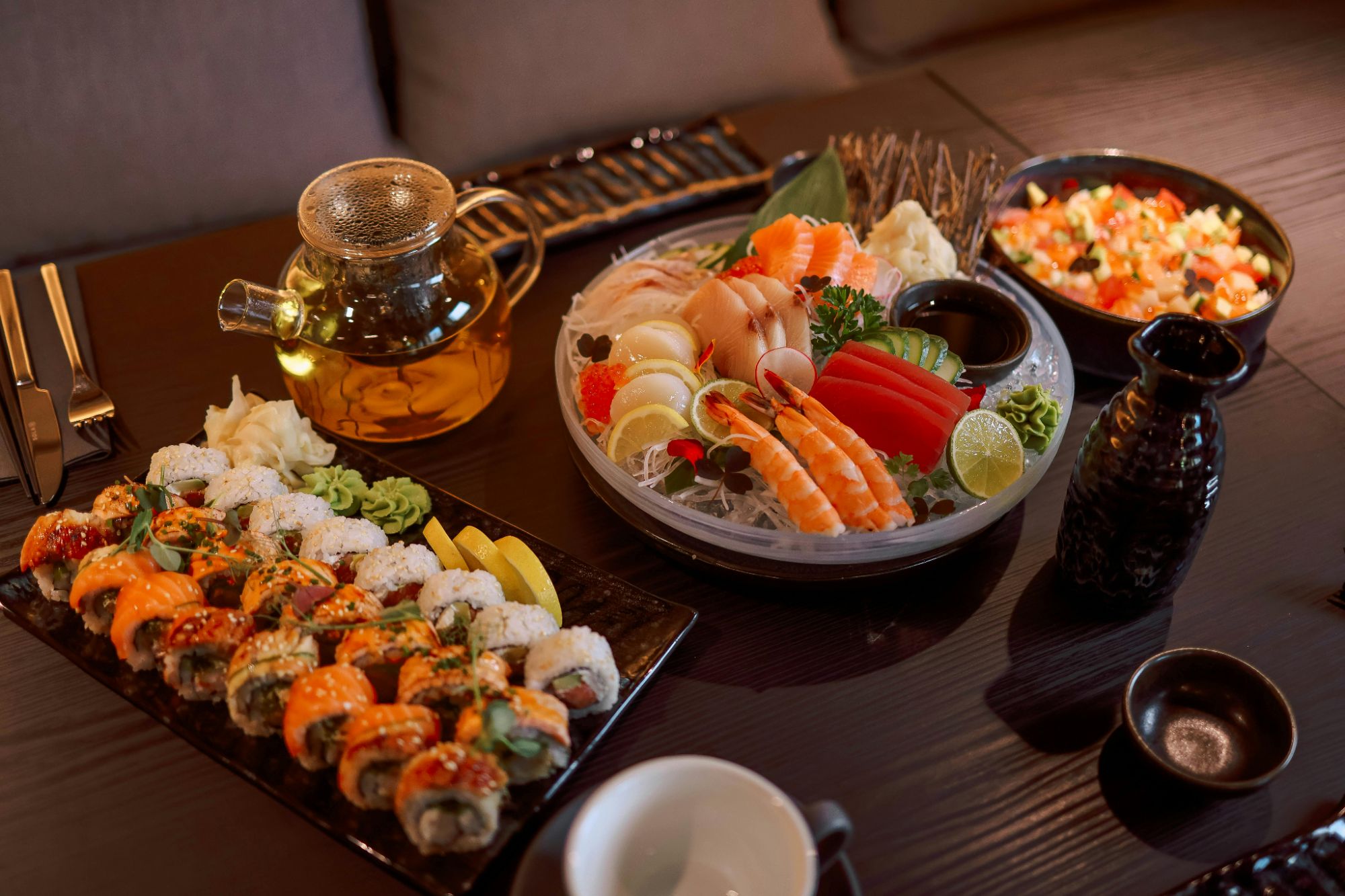 Sushi na czarnym talerzu, sashimi, sałatka owocowa i herbata serwowane na stole w japońskiej restauracji.