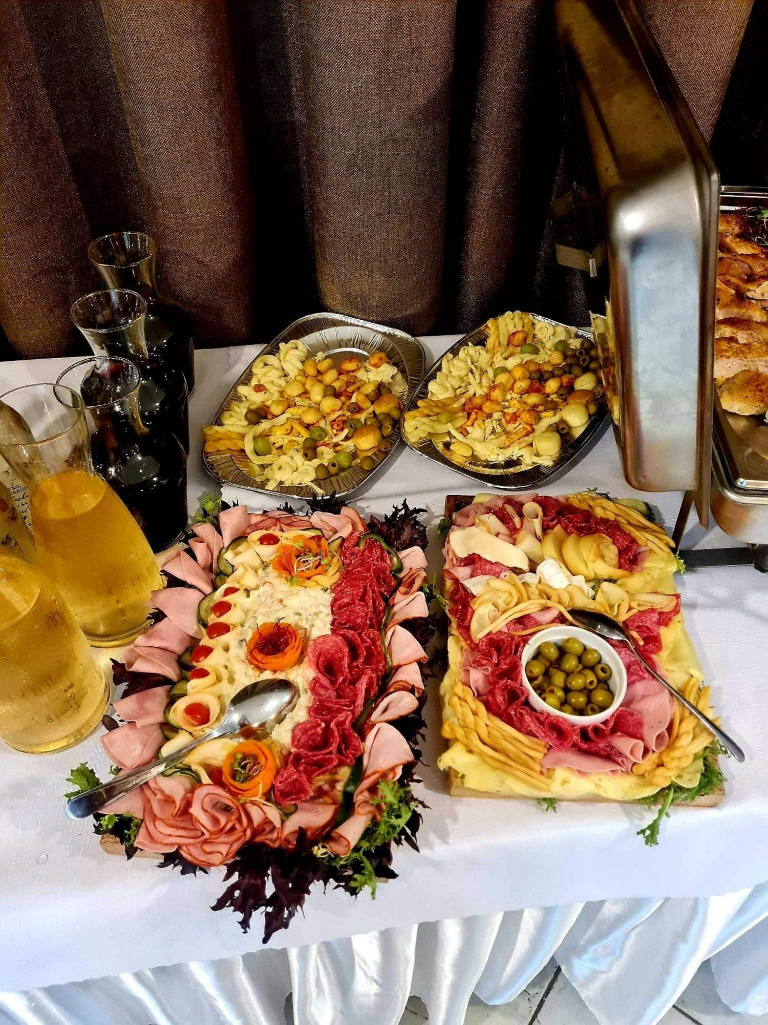 Stol s rôznymi pokrmami, vrátane mäsových a cestovinových šalátov, ozdobený zeleninou.