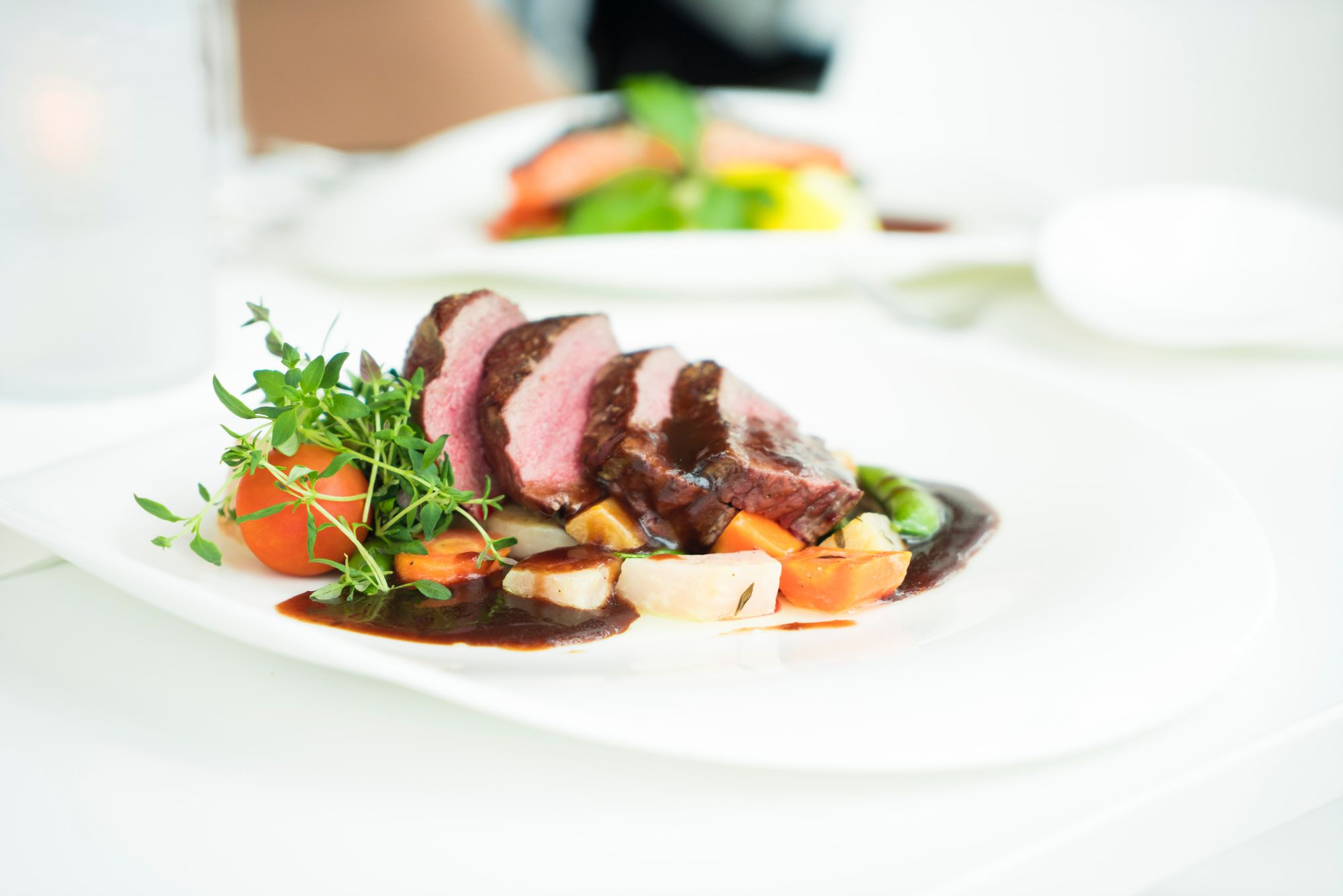 Súprava steak s omáčkou, podávaná so zeleninou a bylinkami na bielom tanieri.
