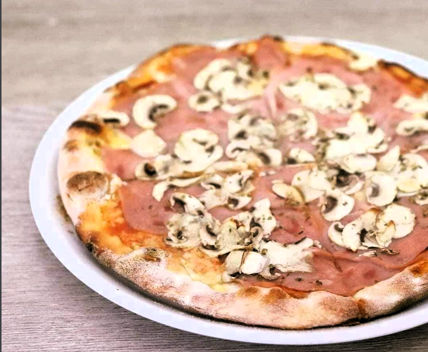 Pizza s šunkom i gljivama na tanjuru.