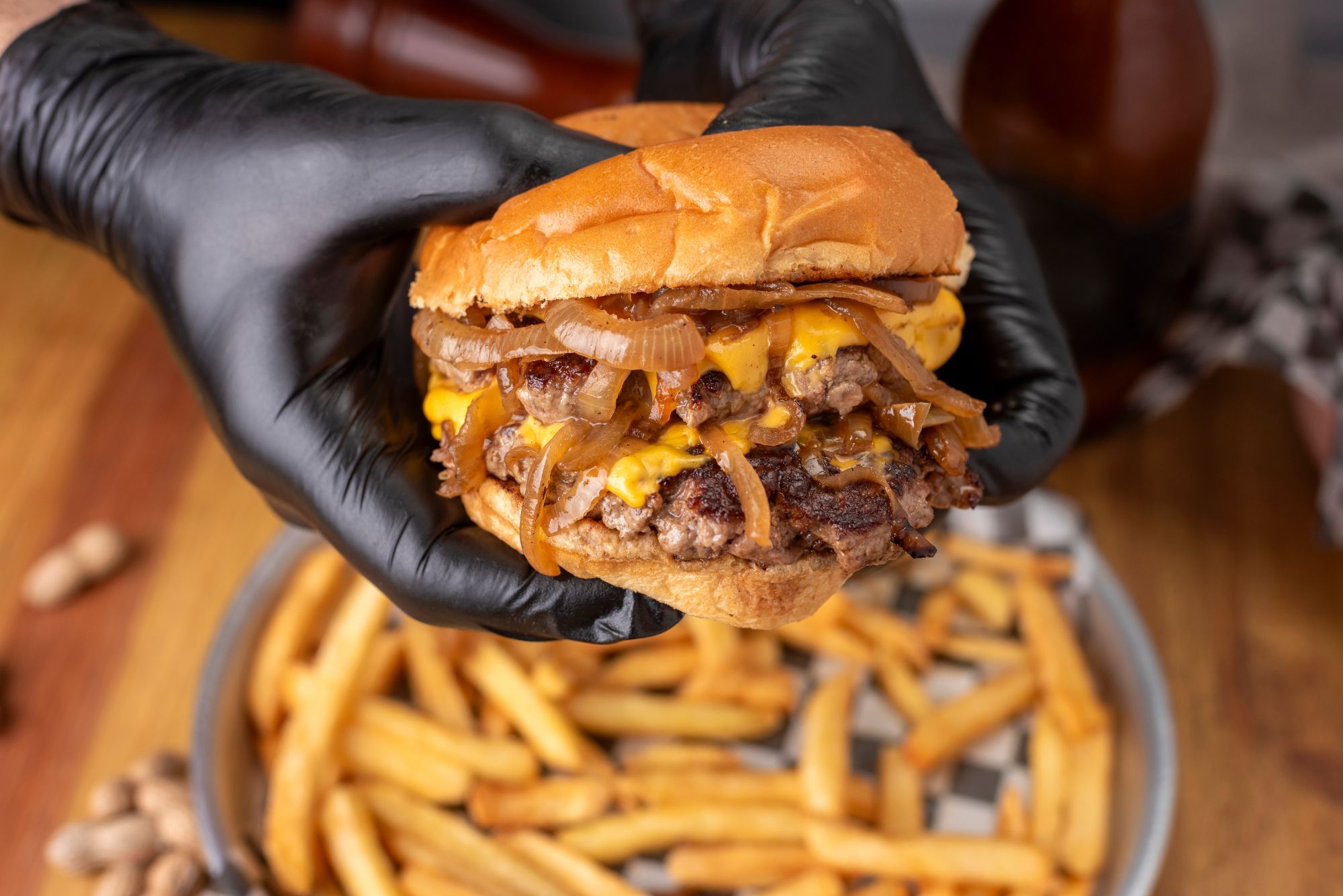 Soczysty burger z serem cheddar, grillowaną cebulą, podawany z frytkami w tle.