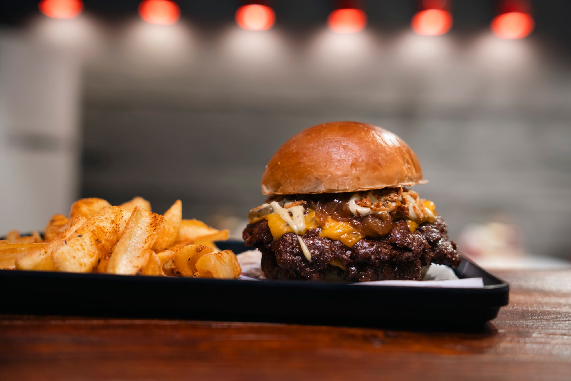 Soczysty burger z serem cheddar i frytkami na talerzu.